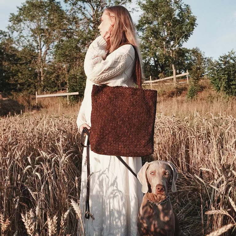 Kvinne i åker med Ribichini Woodstock veske i brunt semsket skinn, håndlaget i flettet design.