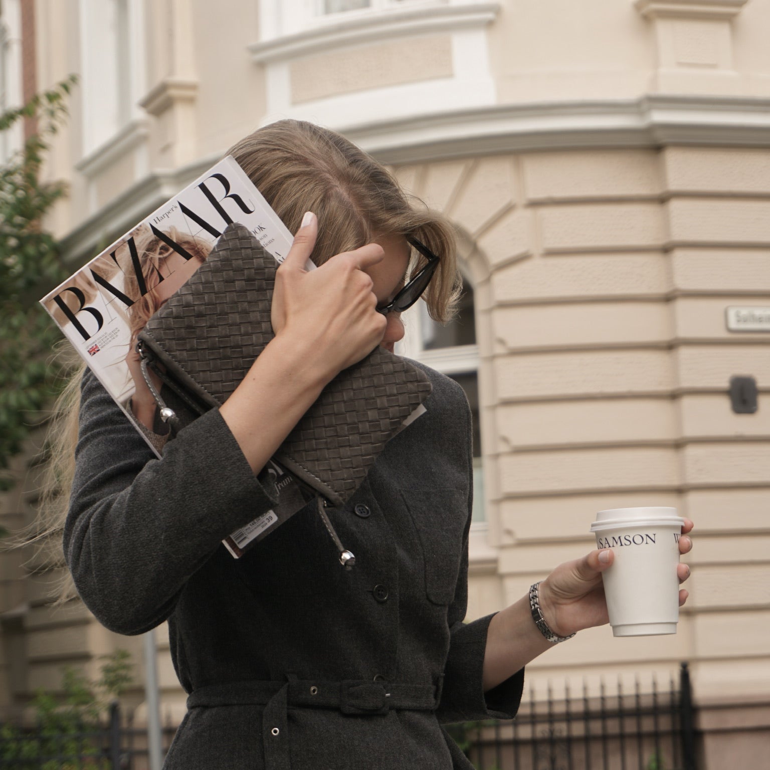Kvinne med Ribichini Camper Clutch i semsket Graphite, Harper’s Bazaar magasin og kaffekopp – elegant business-look.