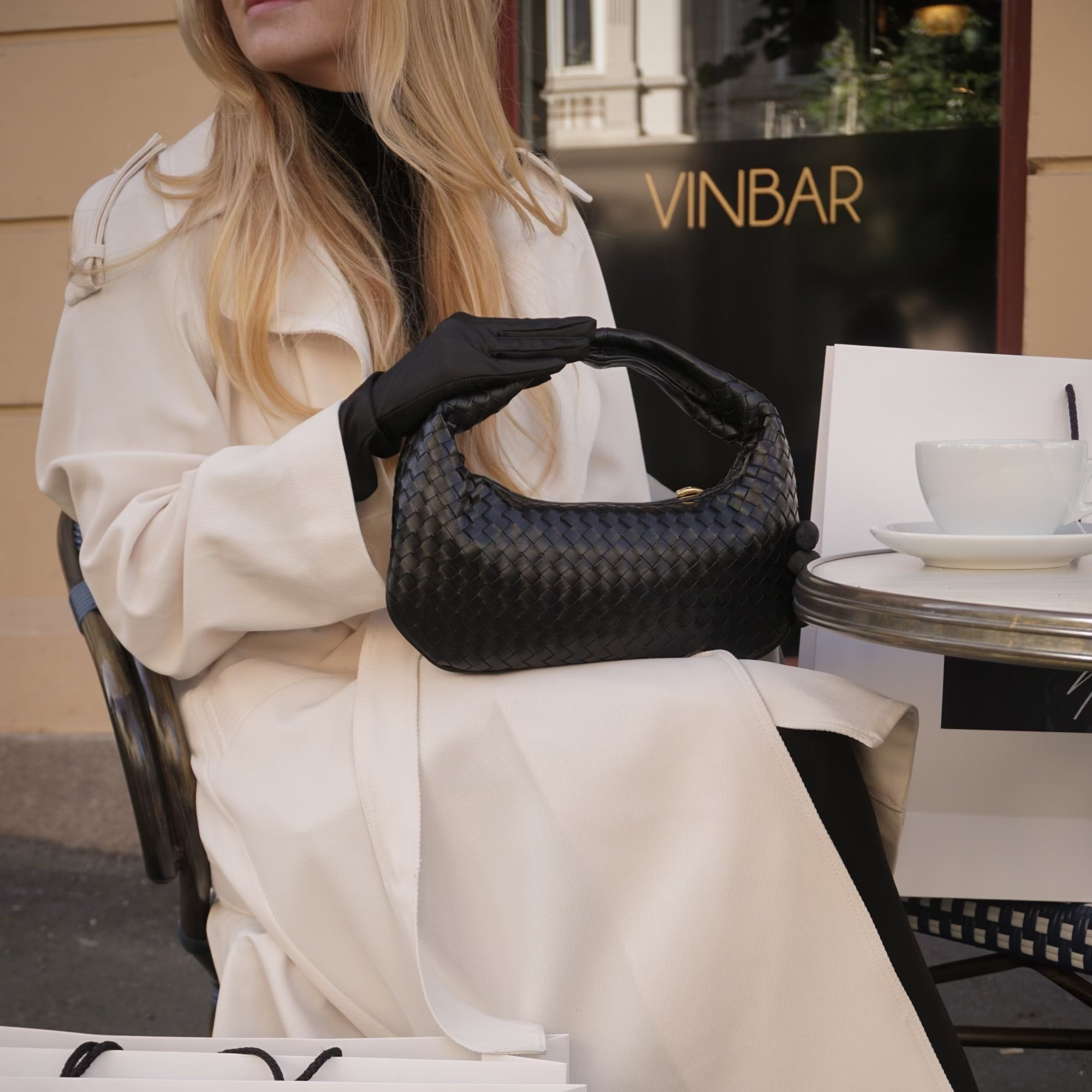 Kvinne holder en Ribichini Isola Bella veske i sort, flettet skinn, et elegant og luksuriøst tilbehør.