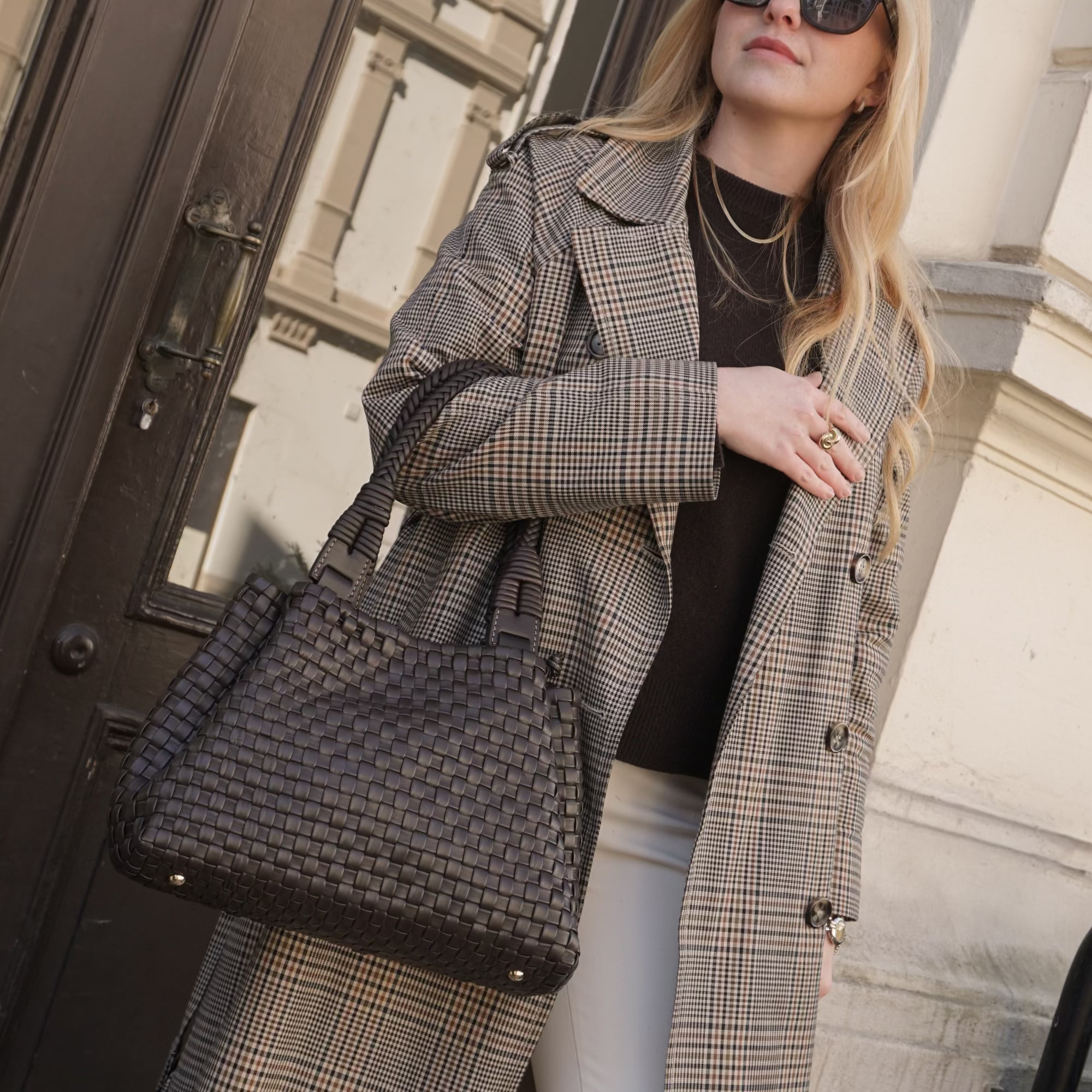 Kvinne i rutete frakk holder en Sophia sjokolade farget flettet veske fra Ribichini over armen