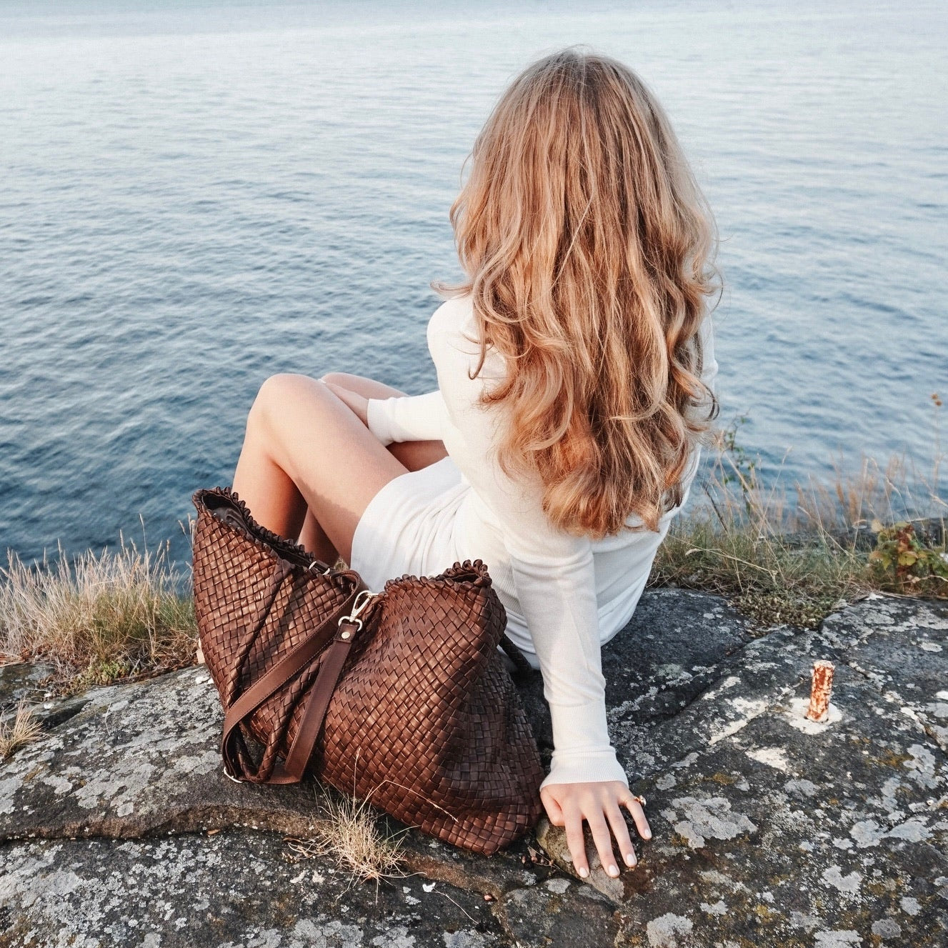 Kvinne i hvit kjole ved sjøen med Ribichini Woodstock Weekend i brun håndflettet skinn.