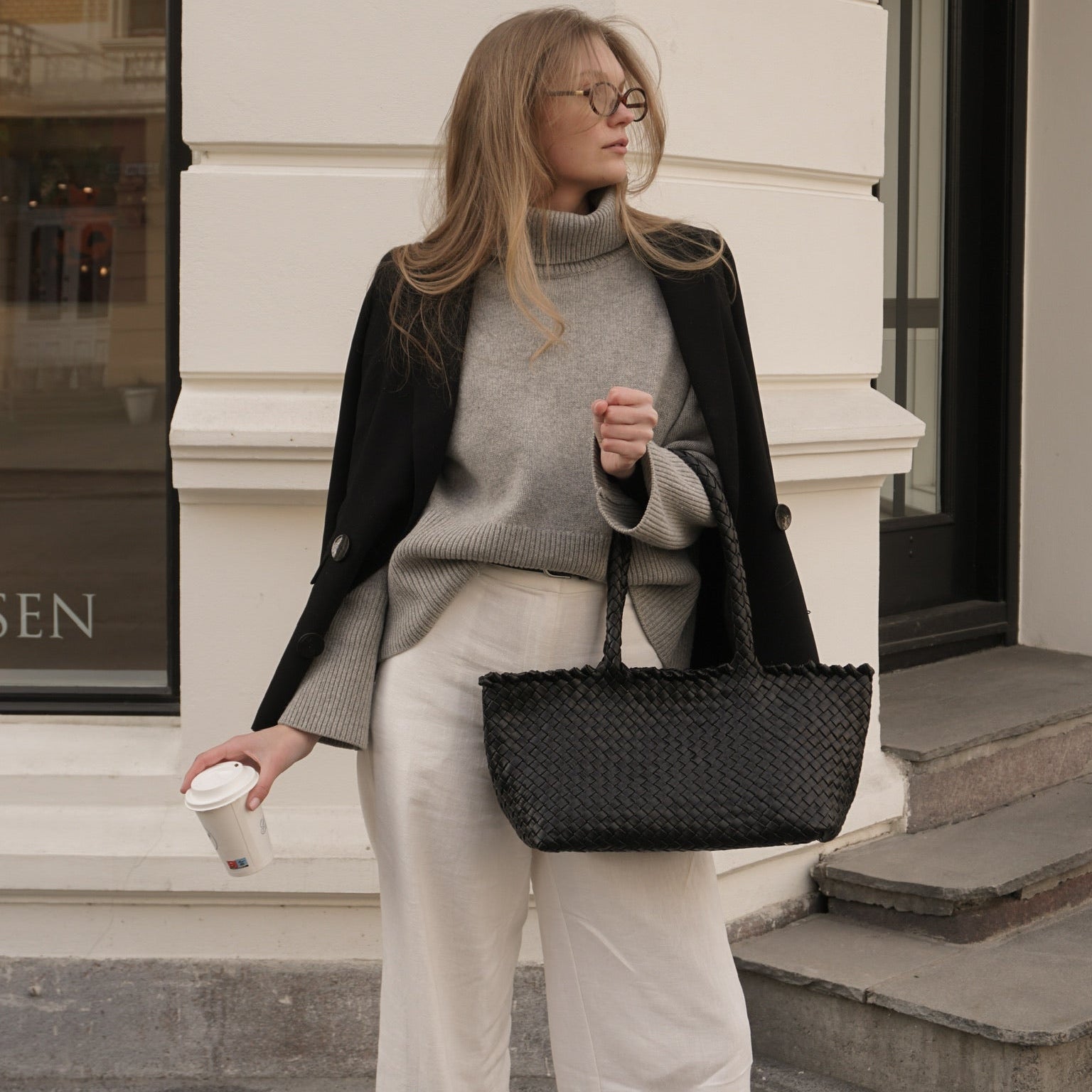 Kvinne med Ribichini Woodstock Classic Babe veske i sort flettet skinn, stylet med blazer og høyhalset genser.