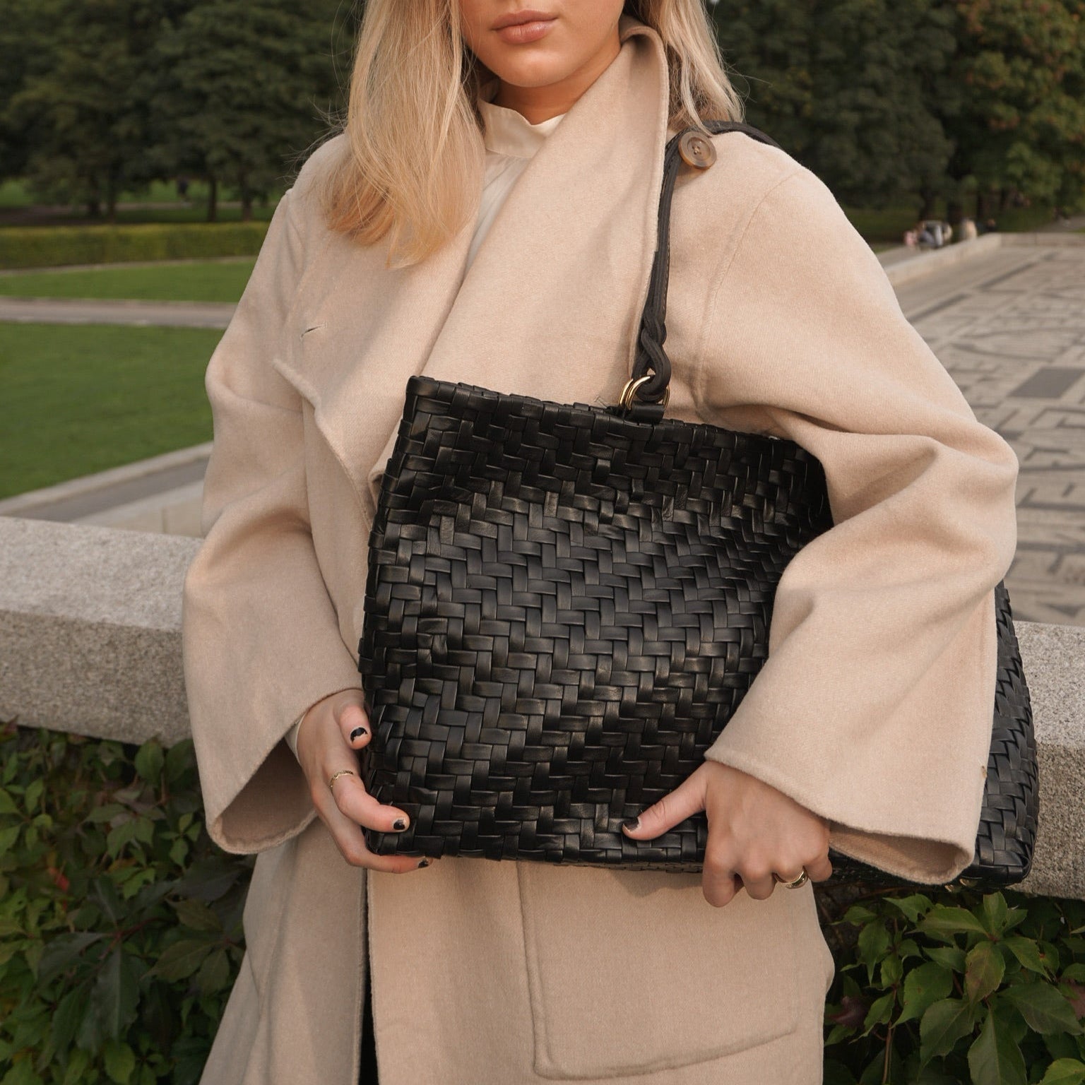 Kvinne i beige kåpe med Ribichini Safari veske i svart flettet skinn – stilfull og tidløs look.