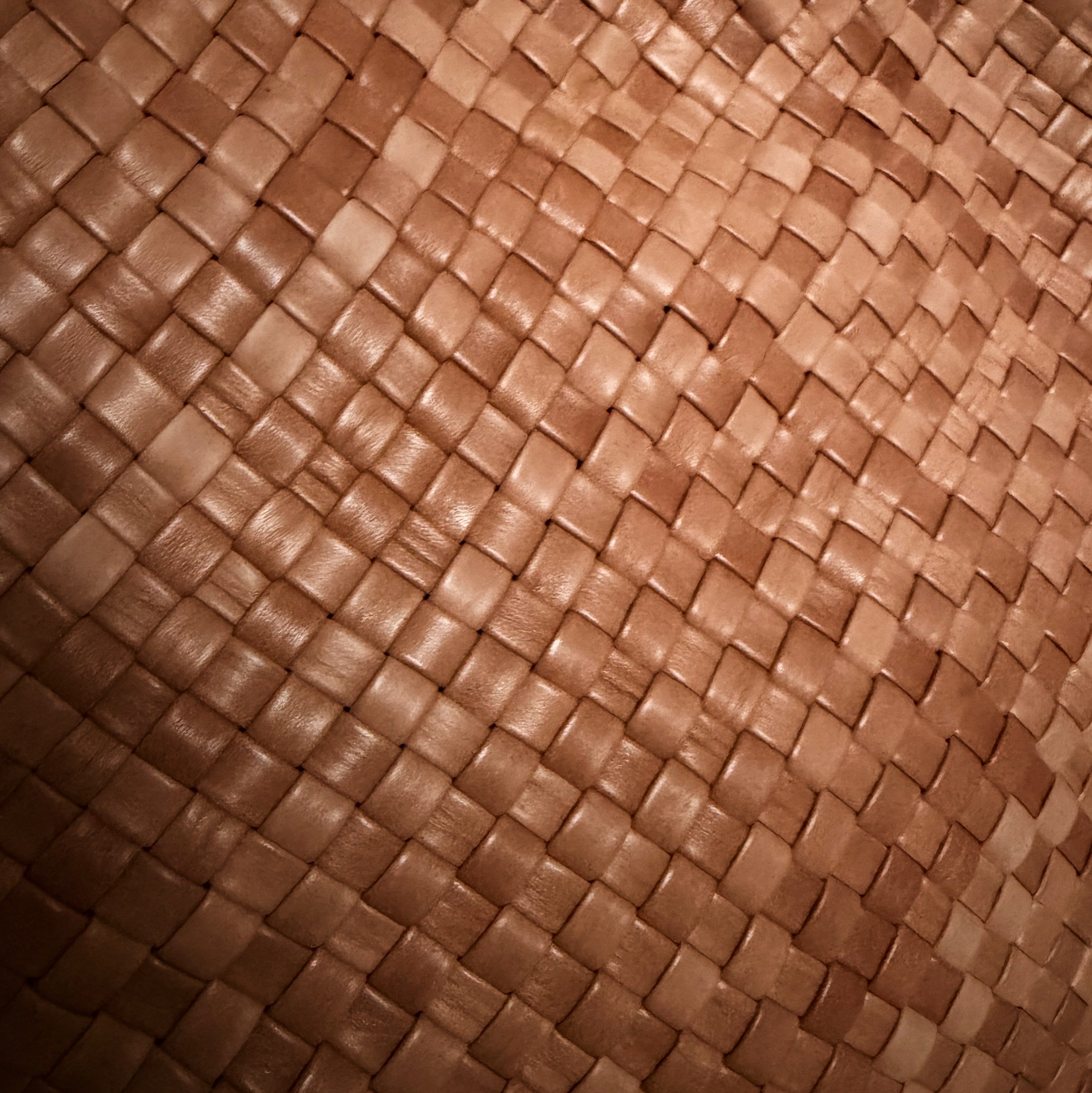 Detaljbilde av håndflettet skinn i cognac med tett flettestruktur.