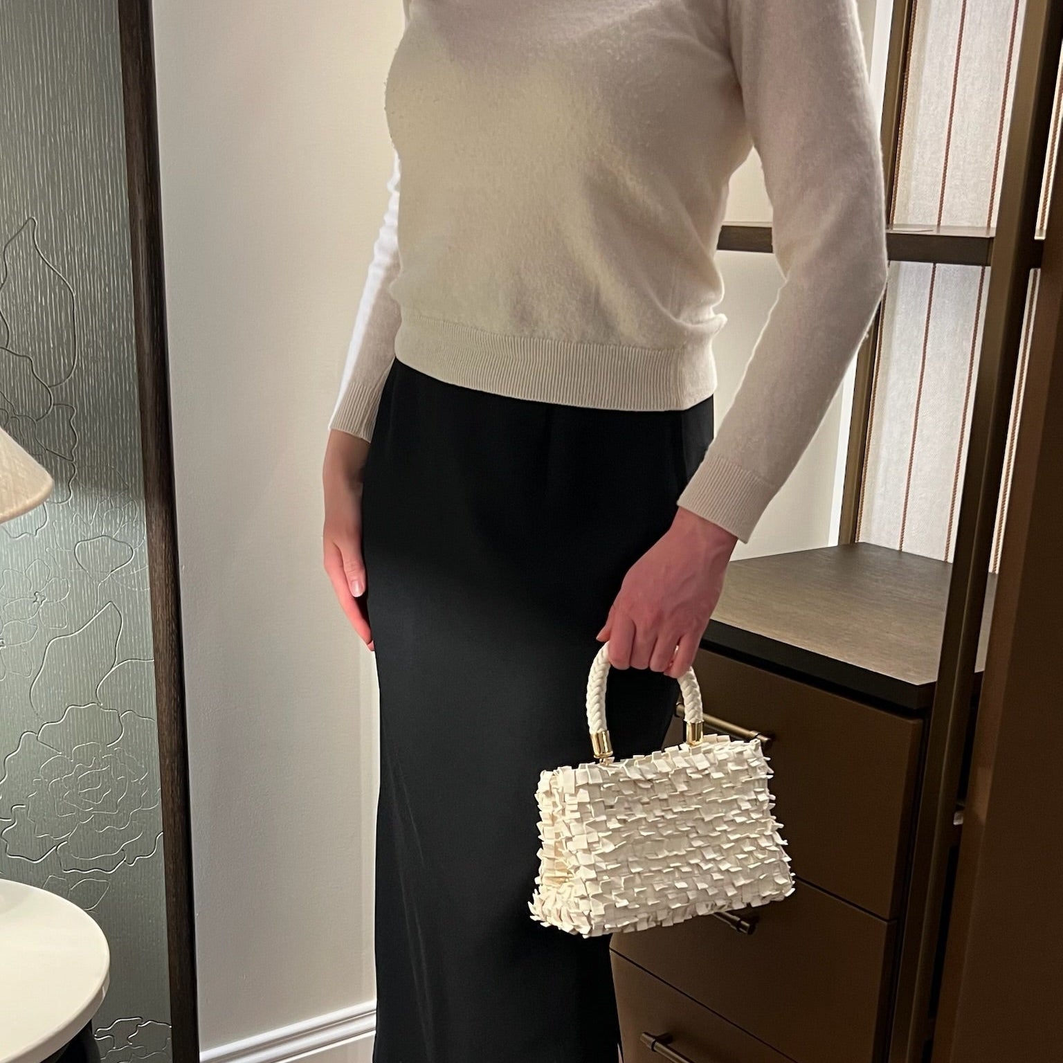 Ribichini Ribimini Cream håndlaget skinnveske i kremfarget lammeskinn, vist med sort skjørt og hvit genser.