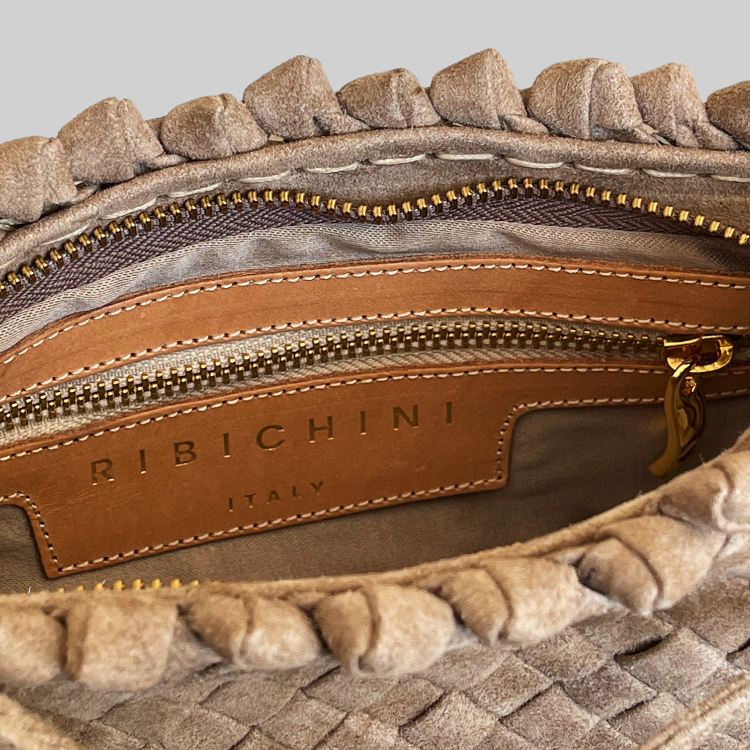 Nærbilde av innsiden på Ribichini Woodstock Royal clutch i terra semsket skinn, med gullglidelås og skinnmerke "Ribichini Italy".