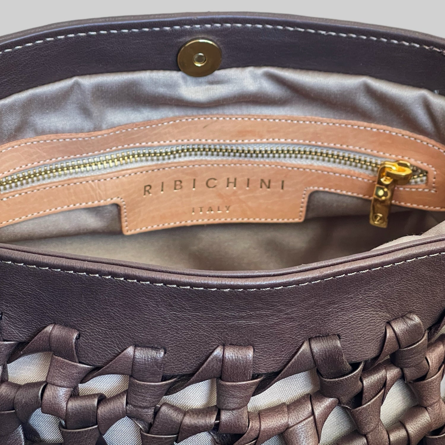 Innsiden av Ribichini Donna-vesken har et silkemykt, fôr og en elegant lærpatch med "RIBICHINI ITALY" i gullskrift. En praktisk glidelåslomme med gyllen glidelås legger til funksjonalitet.