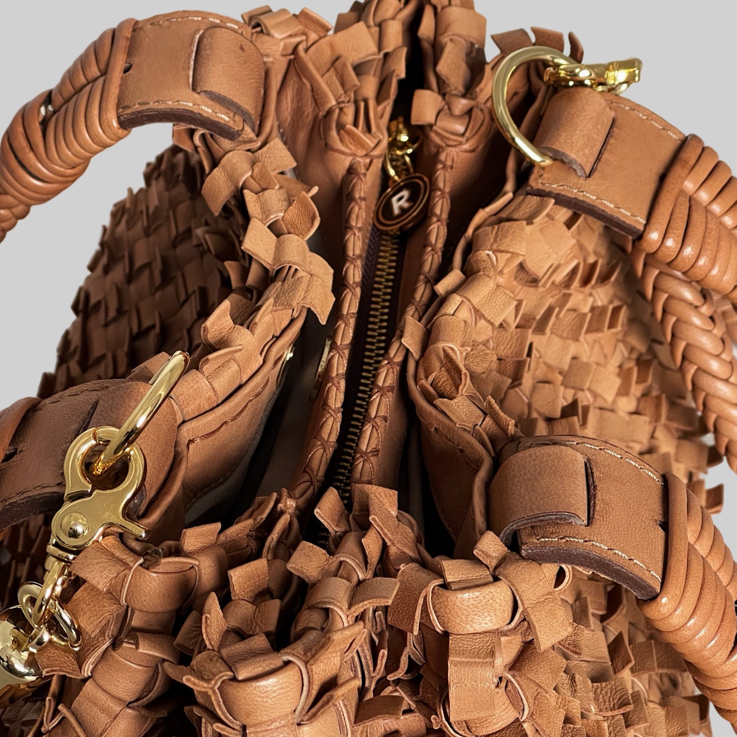 Detalj av Ribichini Loren-vesken i cognac, med plissért skinn, gullfarget glidelås og romslig inndeling for praktisk oppbevaring.