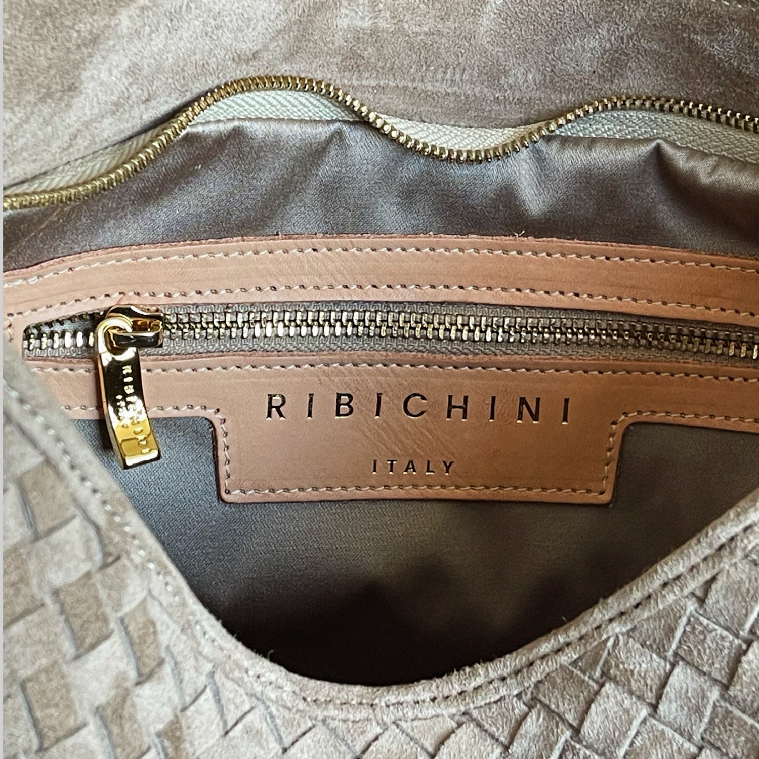 Detalj av innside på Ribichini Saddel-veske med glidelåslomme, gullglidelås og preget logo "RIBICHINI ITALY".