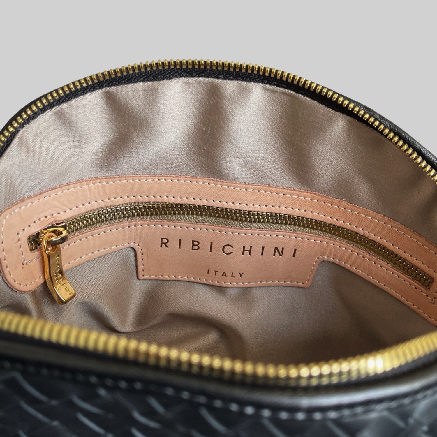 Innside av Ribichini Grande Secrets med beige silkefôr, gullglidelås og preget logo.