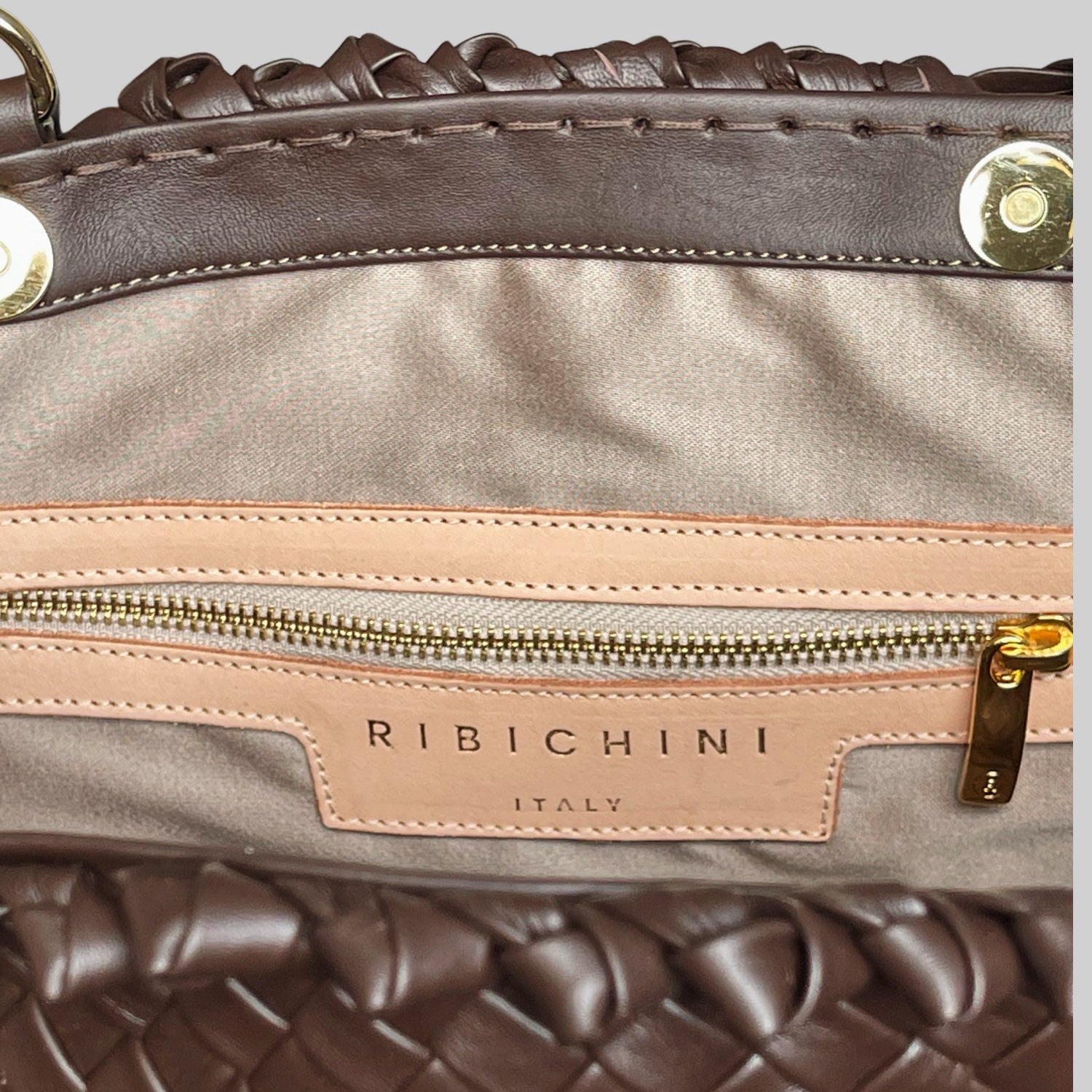 Detaljbilde av innsiden av Woodstock Classic Babe, med beige silkefôr, glidelås med gull-detaljer og Ribichini-logo i skinn.