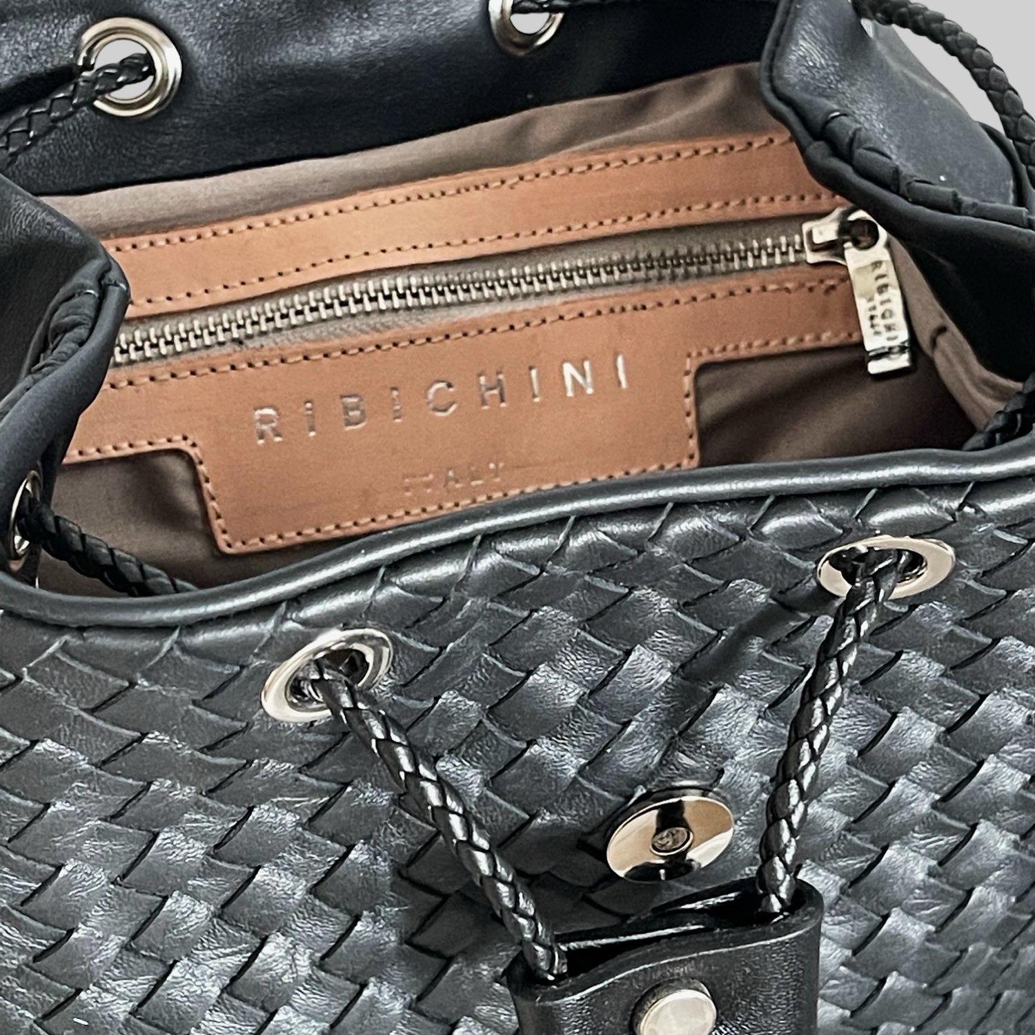 Detaljbilde av innsiden på Ribichini Backpack Mini, med glidelåslomme, skinnfôr og preget Ribichini-logo.