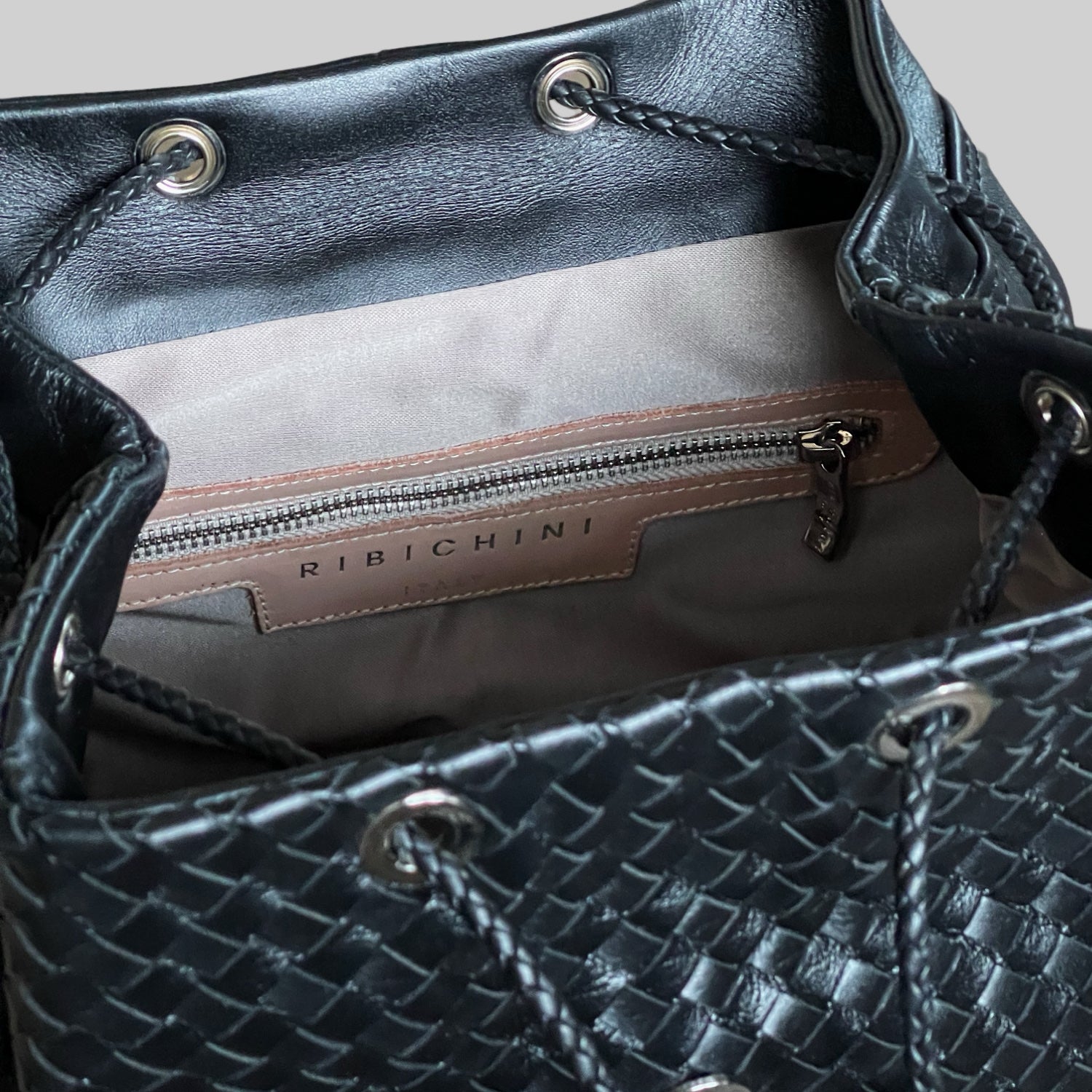 Detaljbilde av innsiden av Ribichini Backpack Large med glidelåslomme og preget logo på skinnetikett.