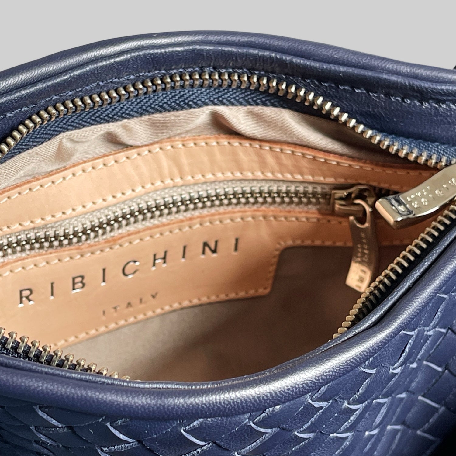 Nærbilde av innside på navyblå Ribichini clutch – skinnfôret med glidelås og preget logo ‘Ribichini Italy’.