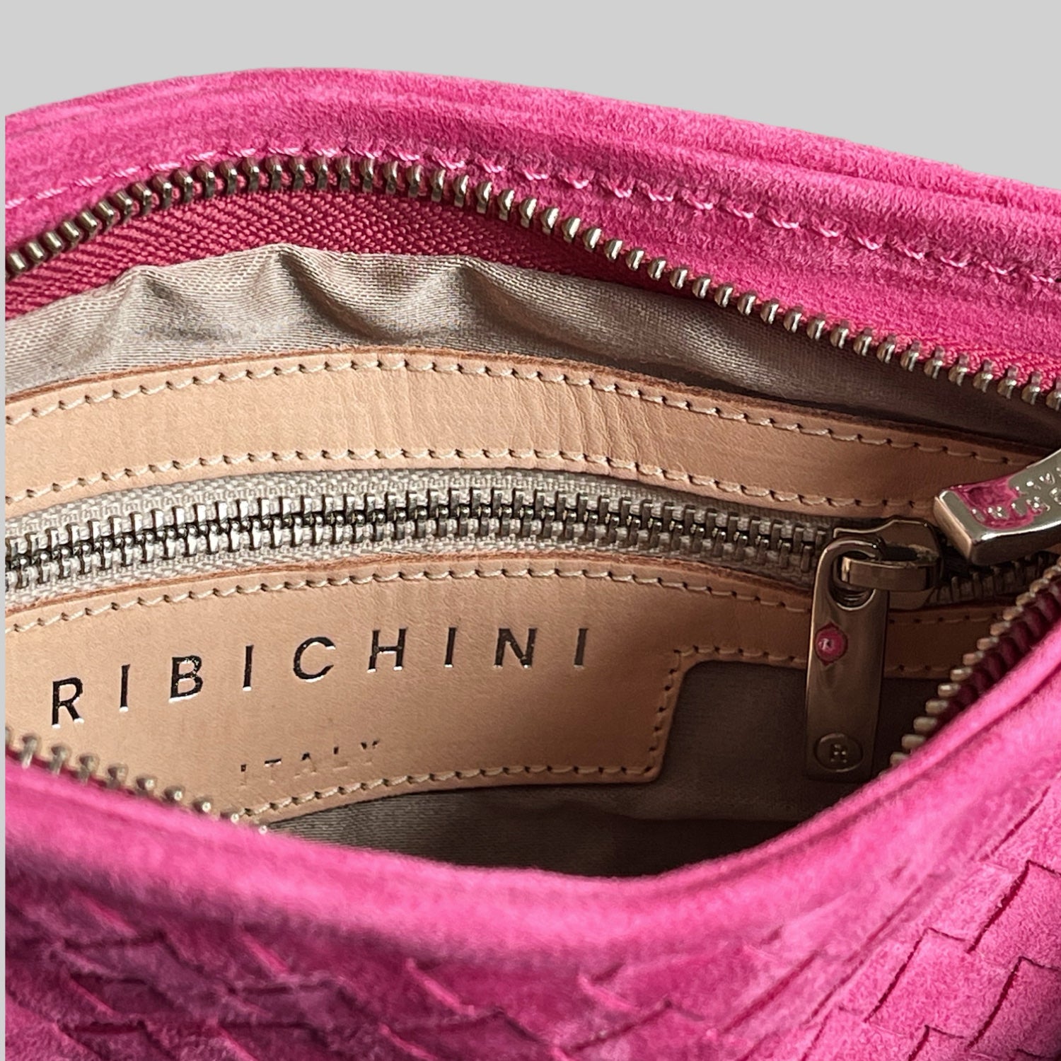 Nærbilde av innsiden på rosa Ribichini clutch – skinnfôr, sølvglidelås og preget ‘Ribichini Italy’-logo.