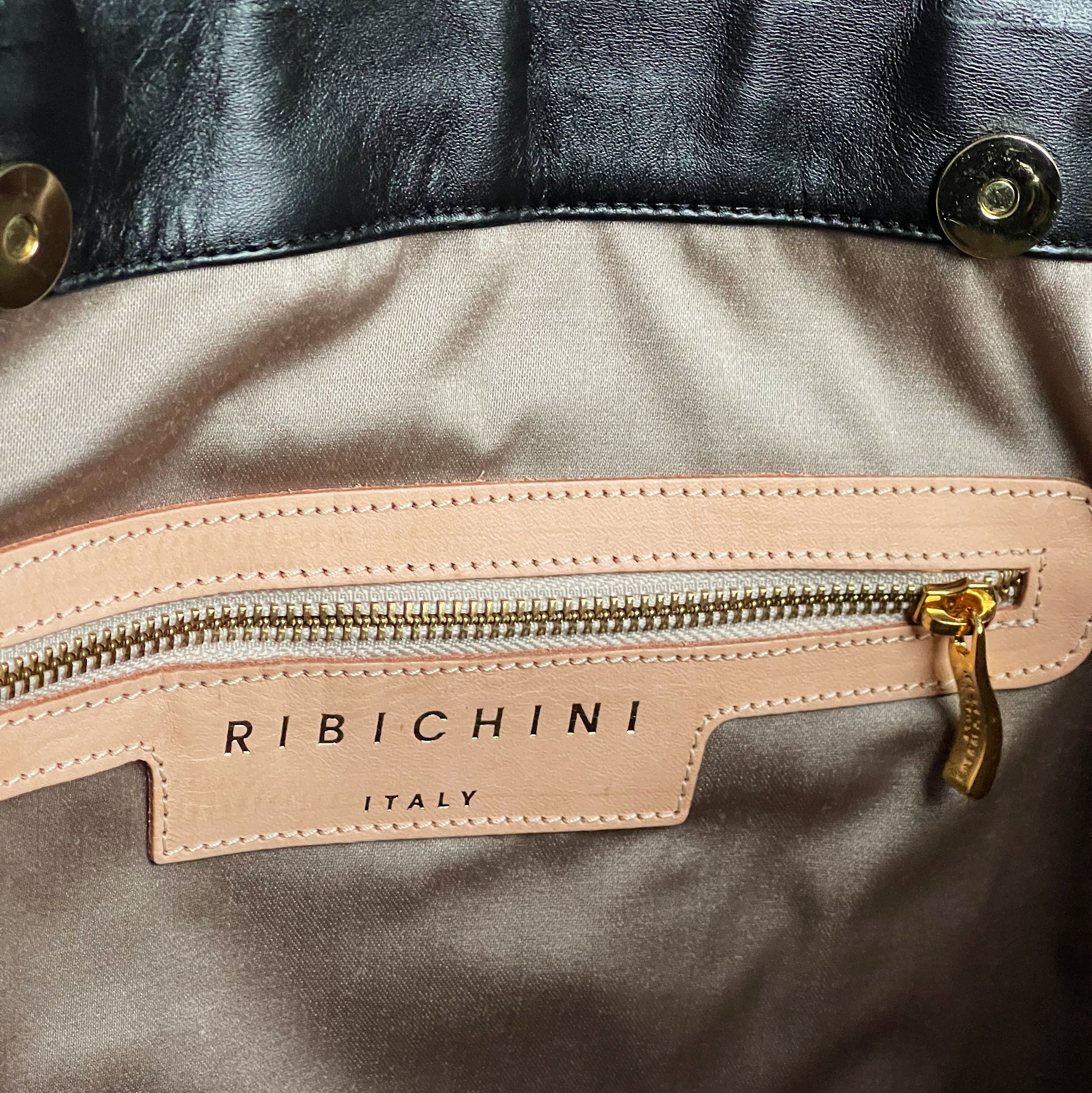 Innvendig glidelåslomme i gullfarge for trygg og organisert oppbevaring. Ikonisk R-logo for ekstra luksus.