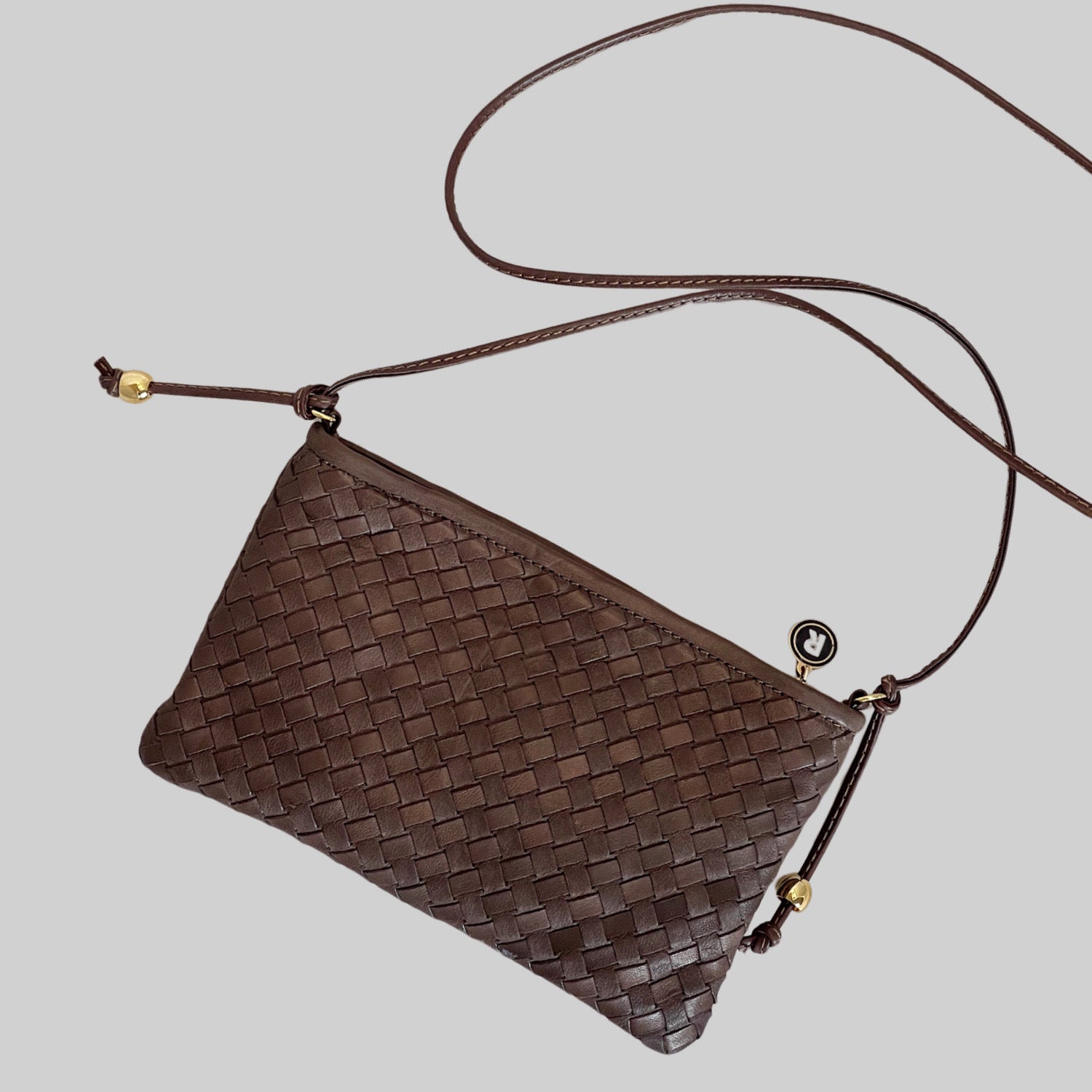 På bildet ser vi en Ribichini Camper Clean Clutch i brunt flettet lammeskinn, elegant plassert i liggende posisjon. De delikate gulldetaljene fremhever det elegante designet, mens den synlige skulderstroppen gir en ekstra dimensjon av stil.