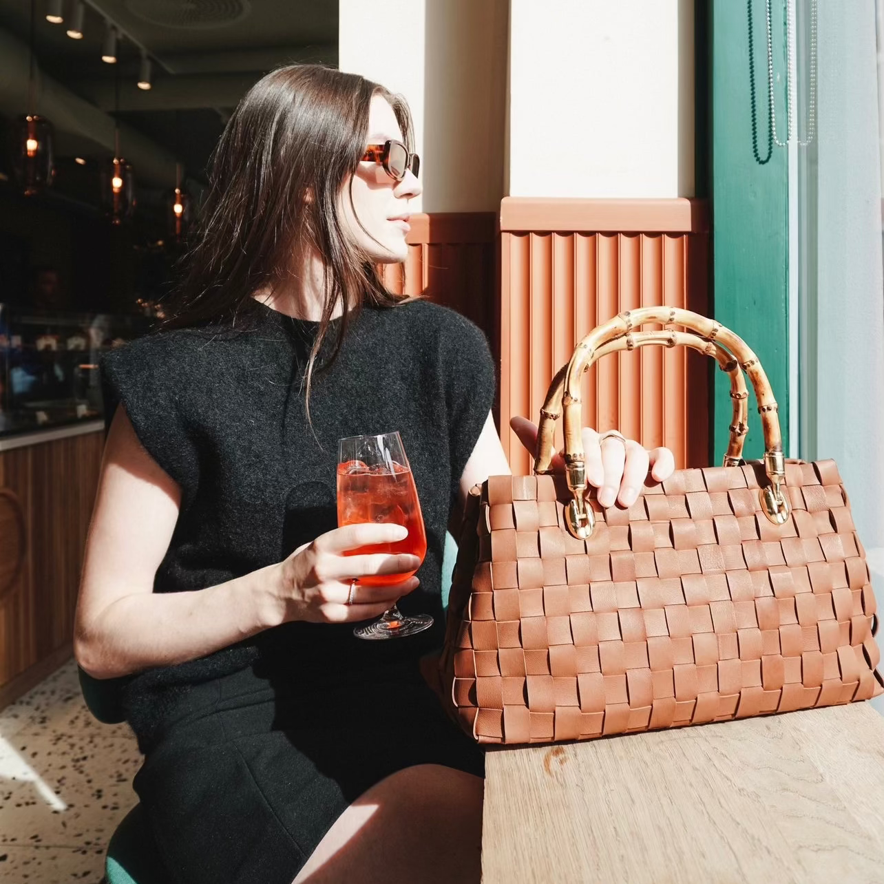 Kvinne på cafe holder en Flettet skinnveske i fargen cognac fra Ribichini med bambus håndtak og gulldetaljer.