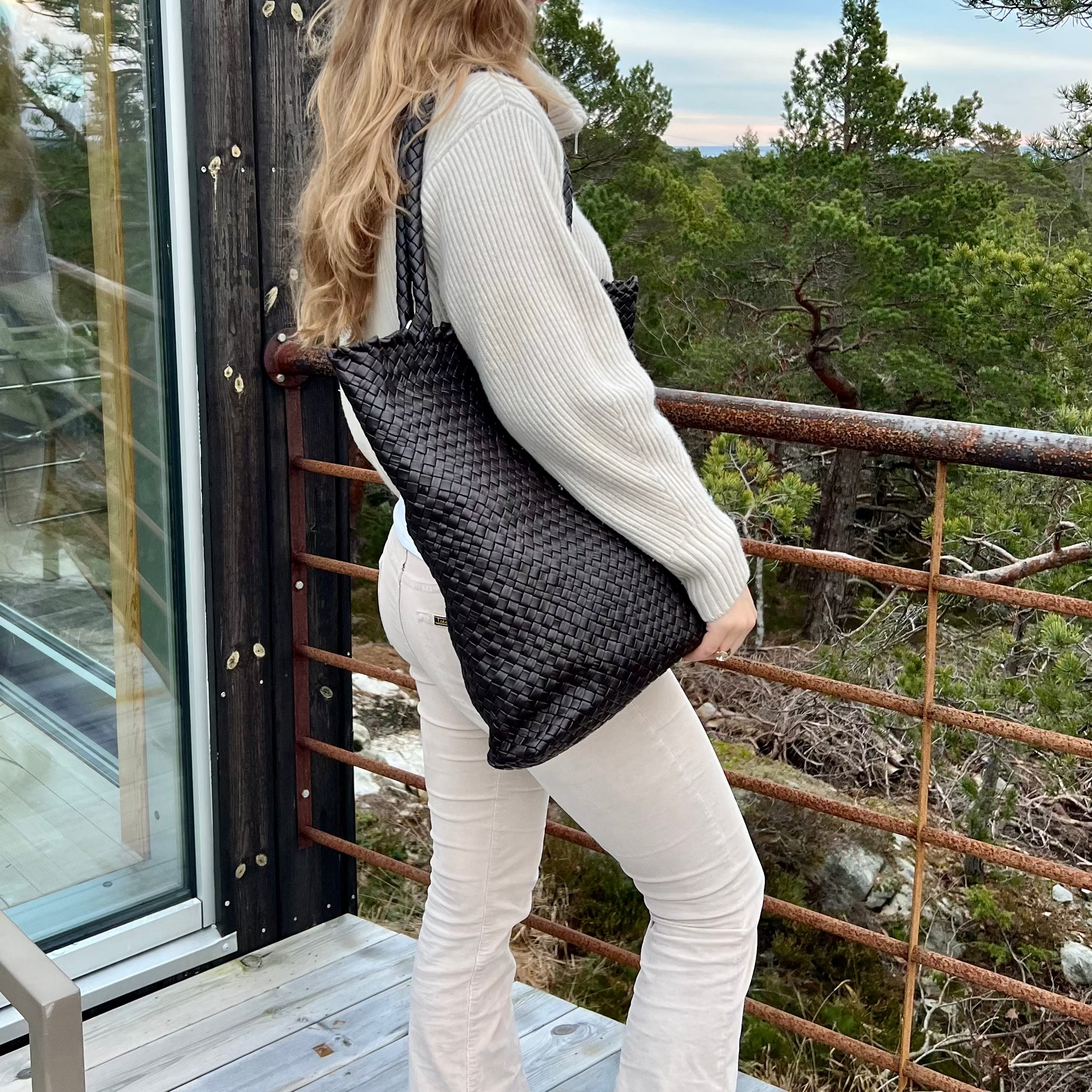 Kvinne bærer over skulderen Ribichini Woodstock i sort er en allsidig flettet skinnveske laget av lammeskinn.