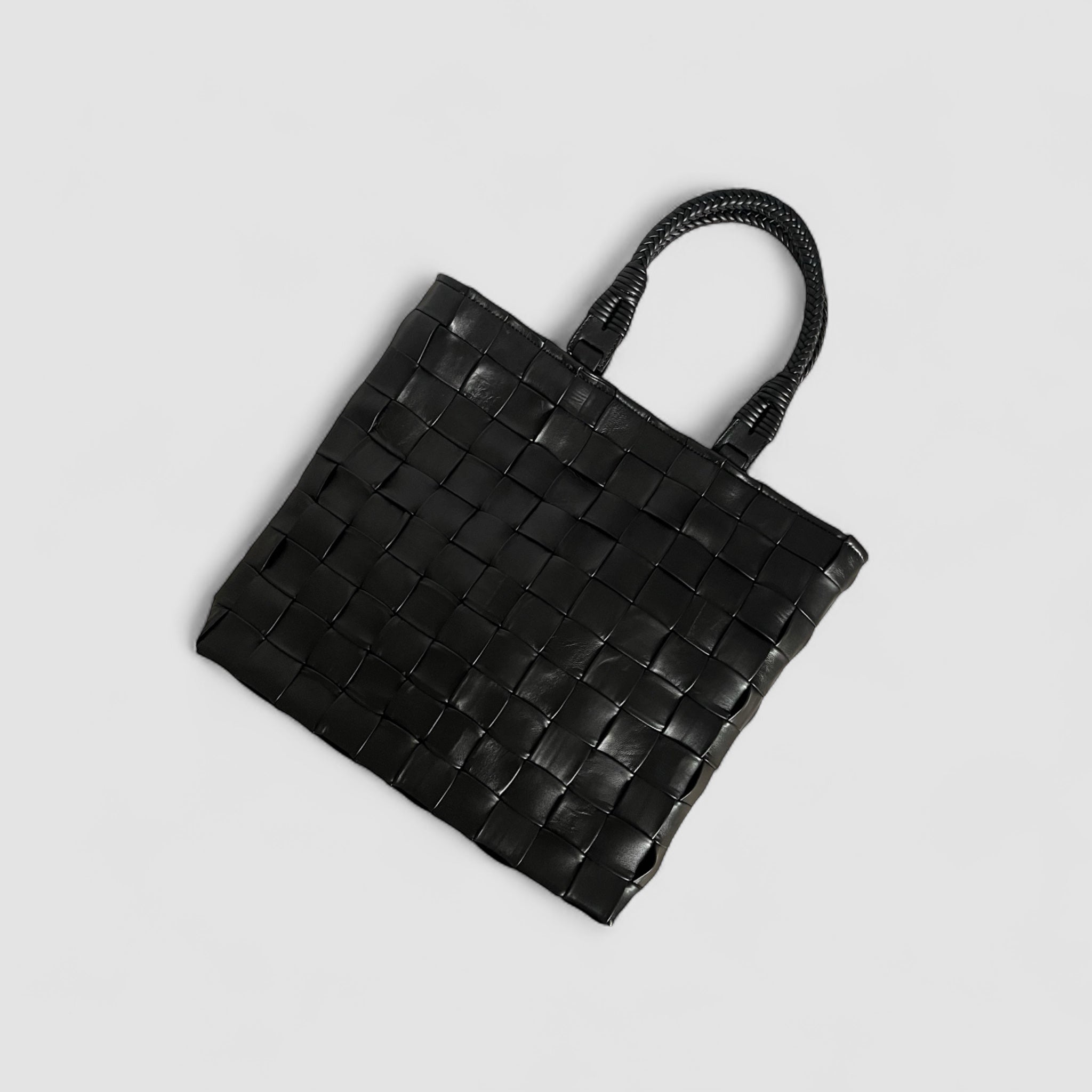 Bildet gir et flott fugleperspektiv av Ribichini Square-vesken i sort. Det håndlagde lammeskinnet og de flettede rutene.