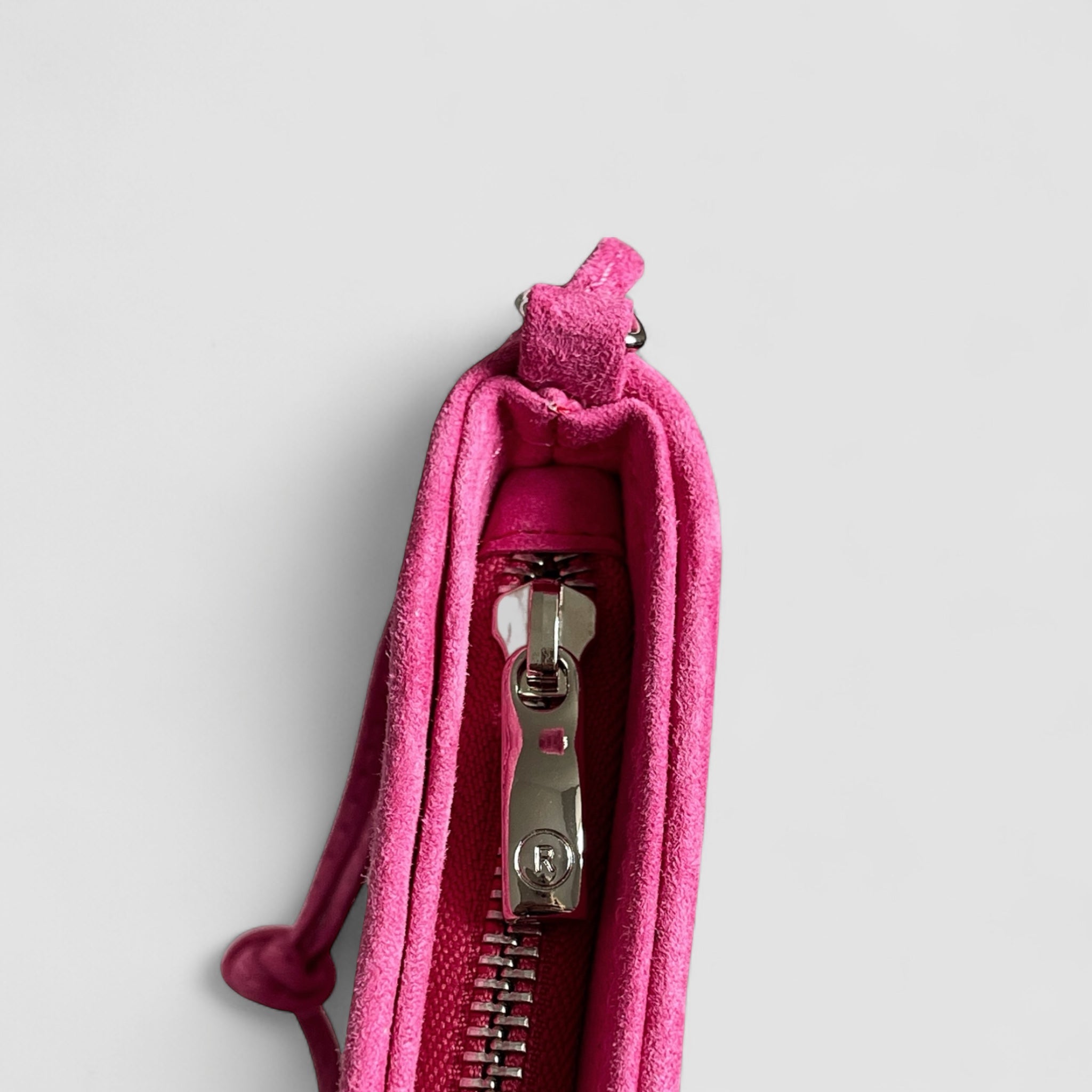 Detaljbilde av sølvglidelås med preget R-logo på rosa Ribichini clutch i semsket lammeskinn.