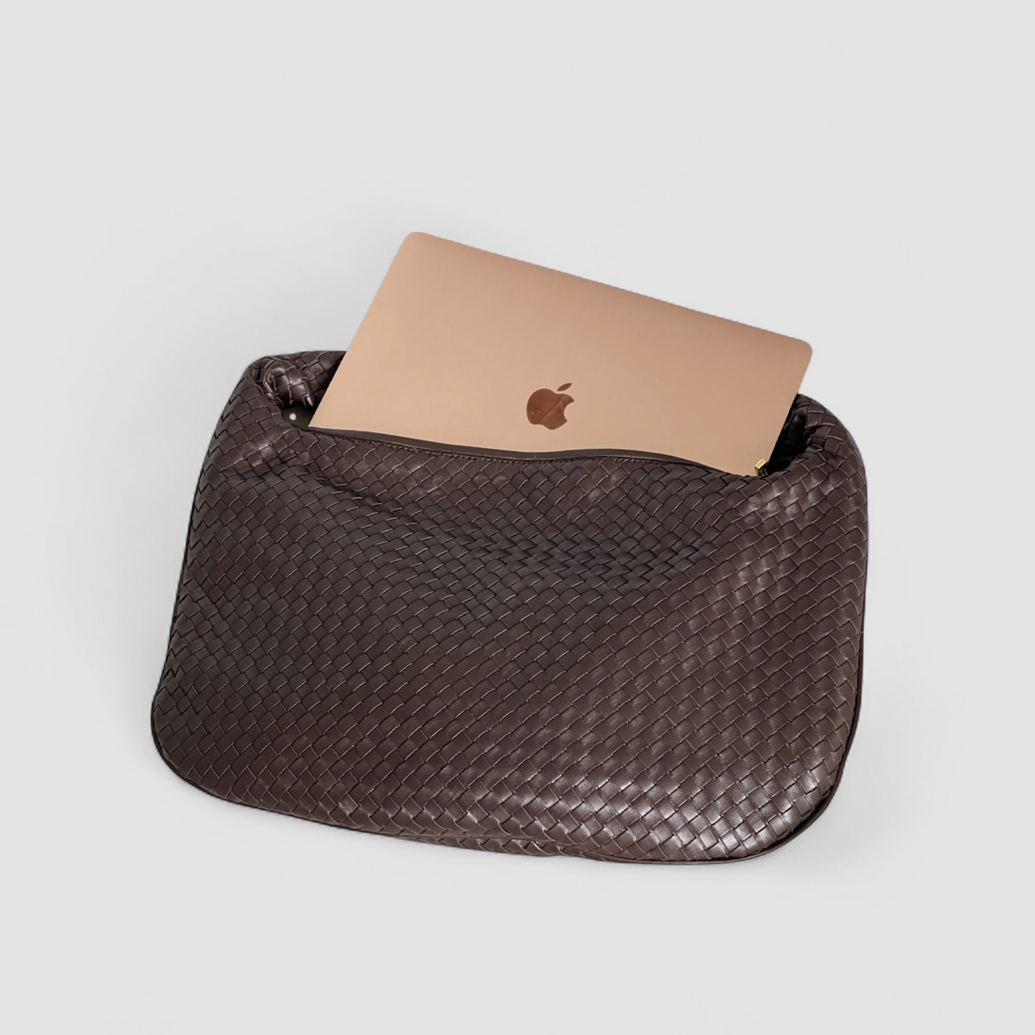 Ribichini Isola skinnveske i sjokolade med flettet design, med plass til en bærbar datamaskin som stikker opp fra vesken.