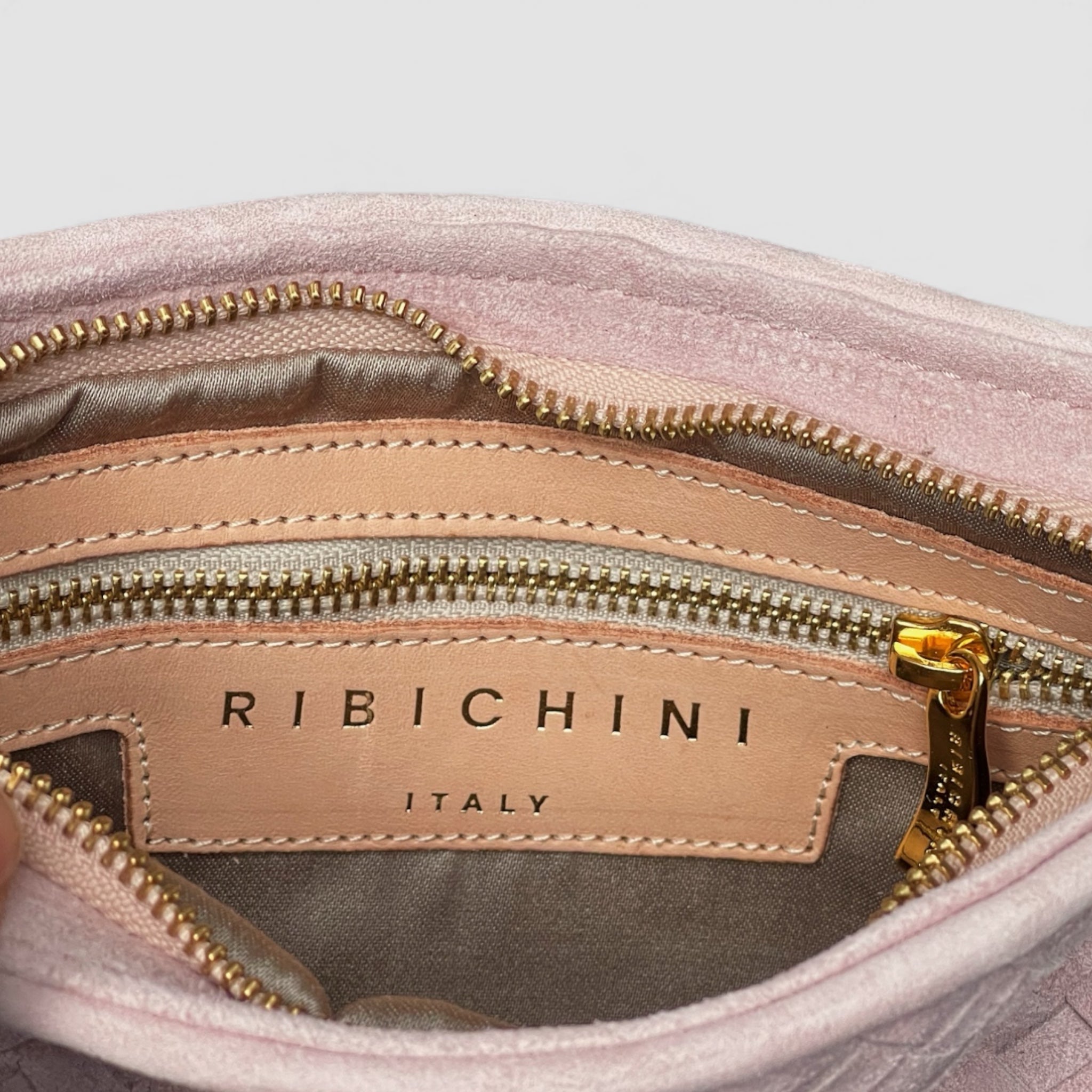 Nærbilde av innsiden av Ribichini Camper Clutch i Rosa med gullfarget glidelås og logo preget i skinnet.