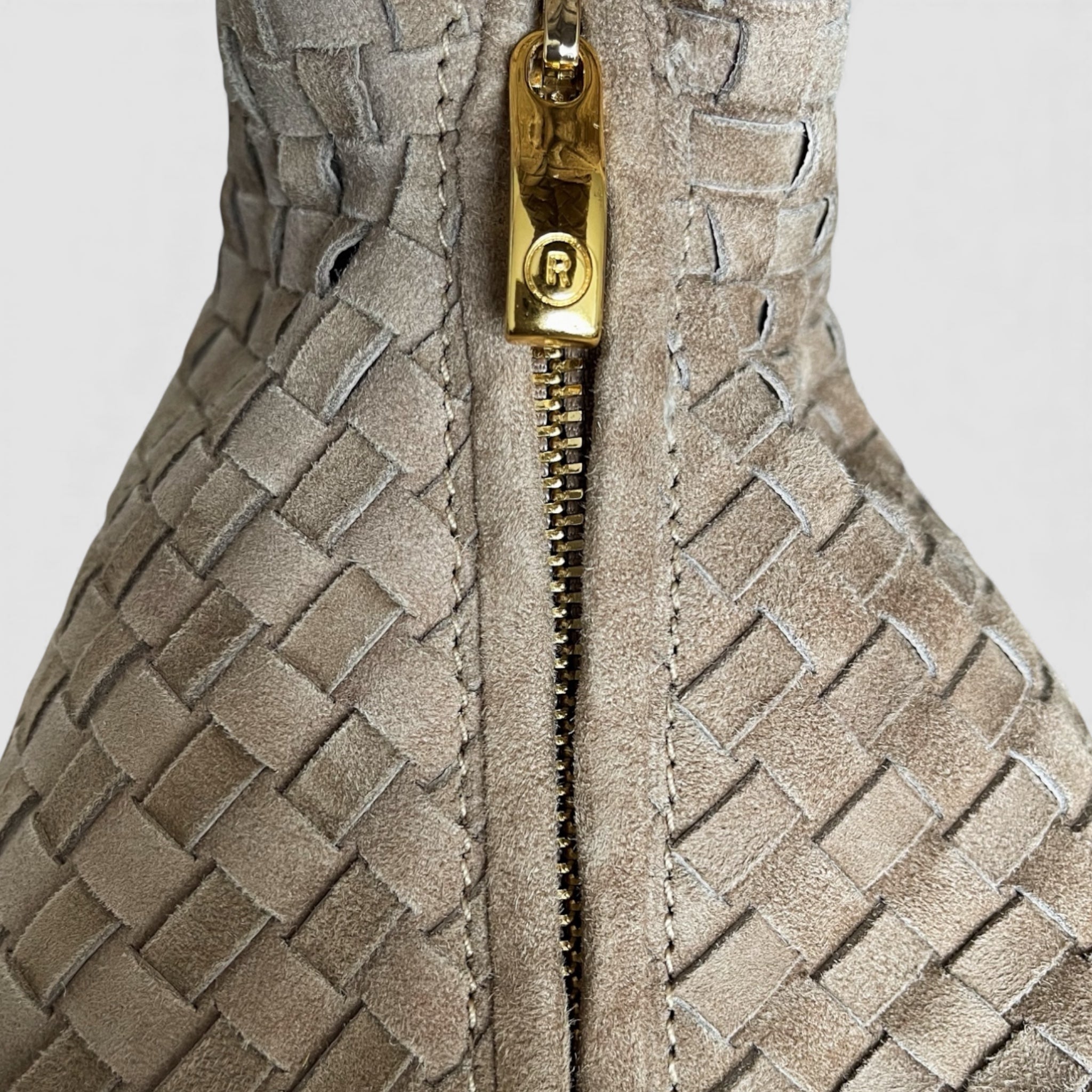 Detaljert bilde av Ribichini-veskens glidelås i gull med merkevarelogoen R, mot flettet semsket lammeskinn.