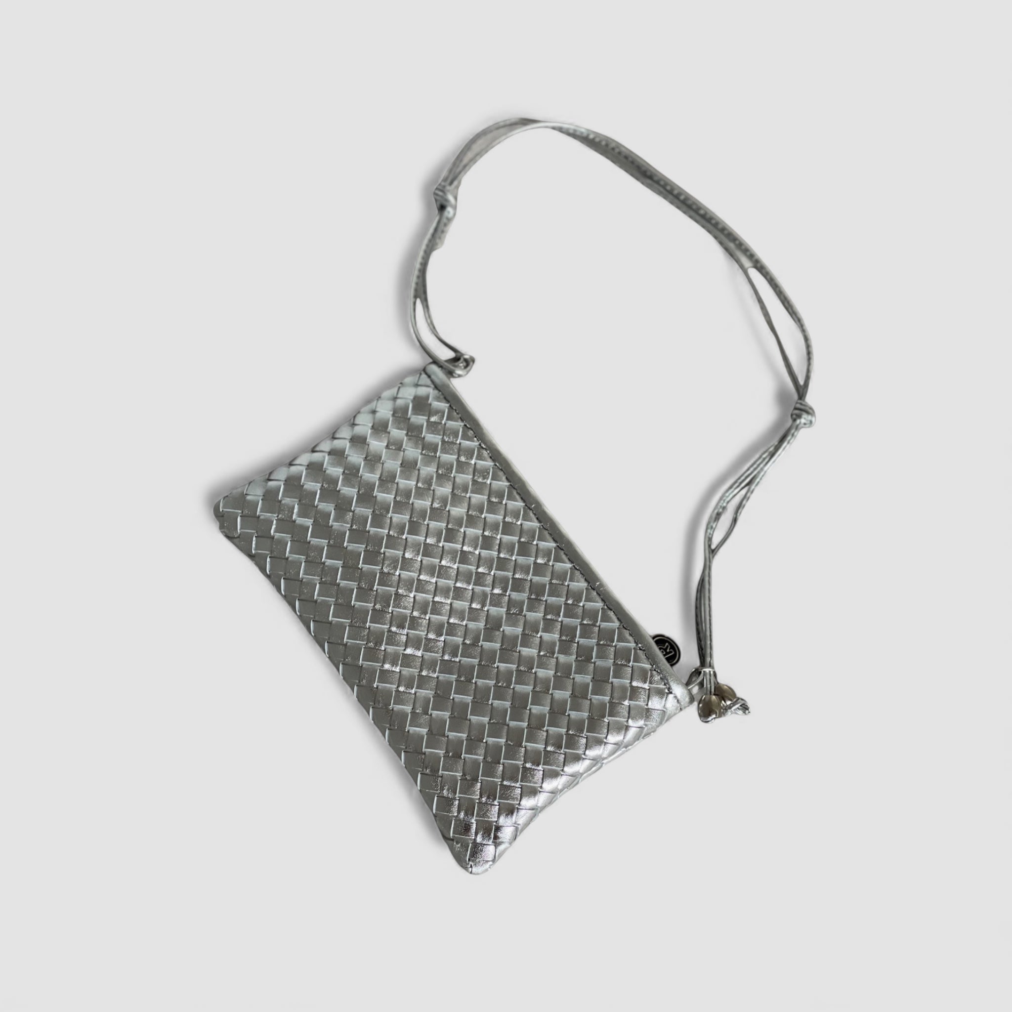 Ribichini Camper Clean clutch i strålende sølv, hvilende i en liggende posisjon, viser den håndlagde flettede lammeskinn og slående sølvdetaljer.