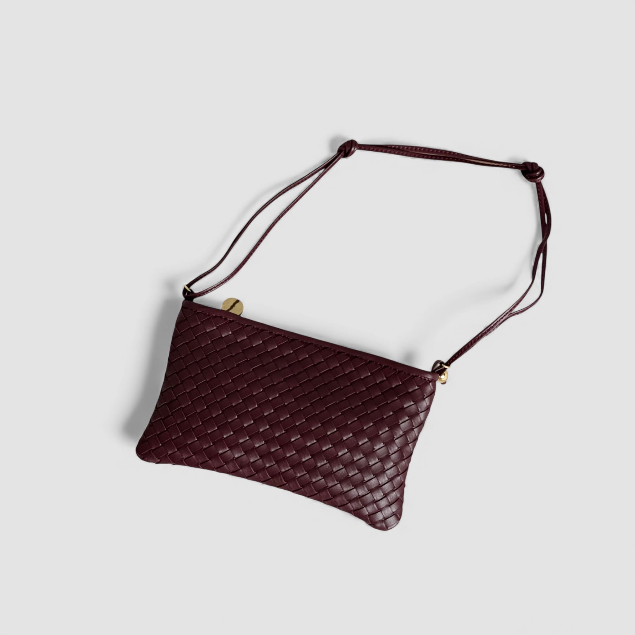 Ribichini Camper Clean clutchen i bordeaux ligger elegant med synlige gulldetaljer og en flettet tekstur, klar til å bæres over skulderen.