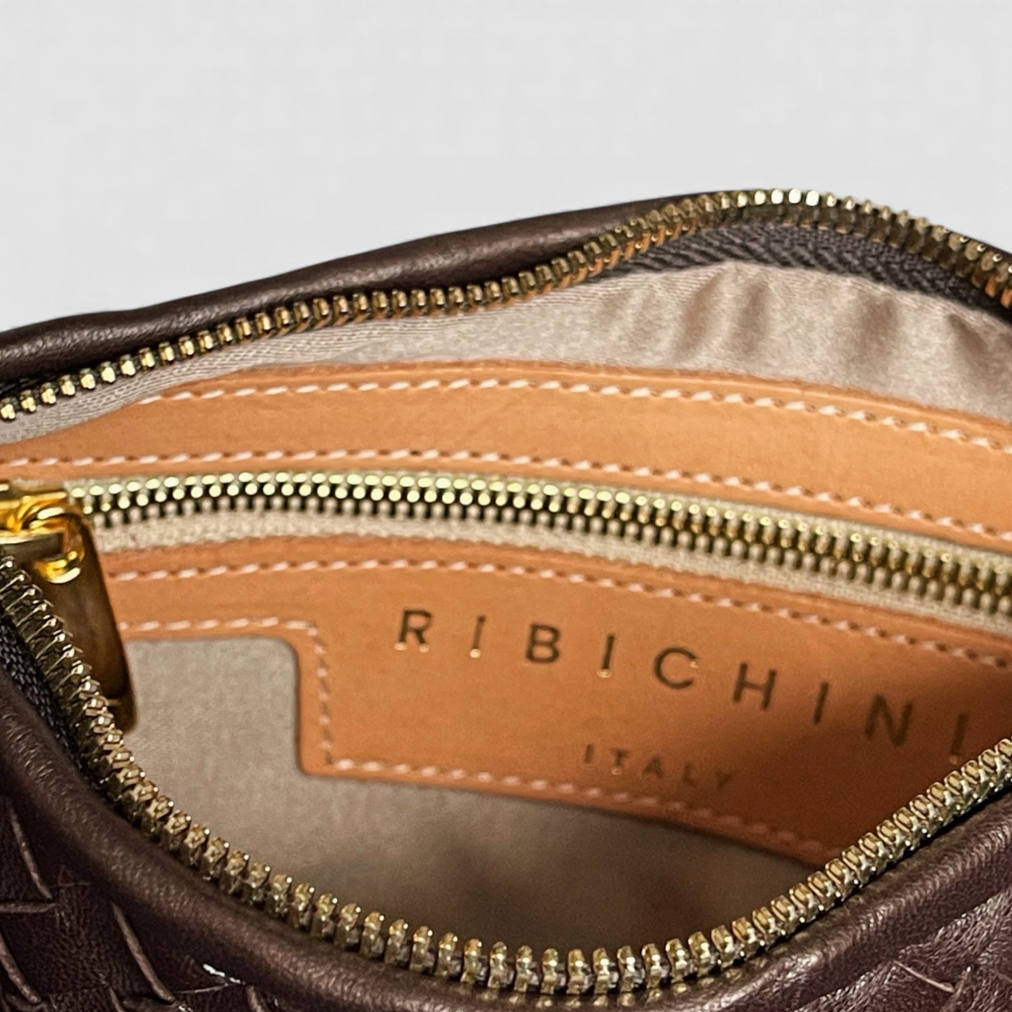 Nærbilde av interiøret på en Ribichini Isola Bella veske, med gullglidelås og skinnmerke som viser "Ribichini Italy