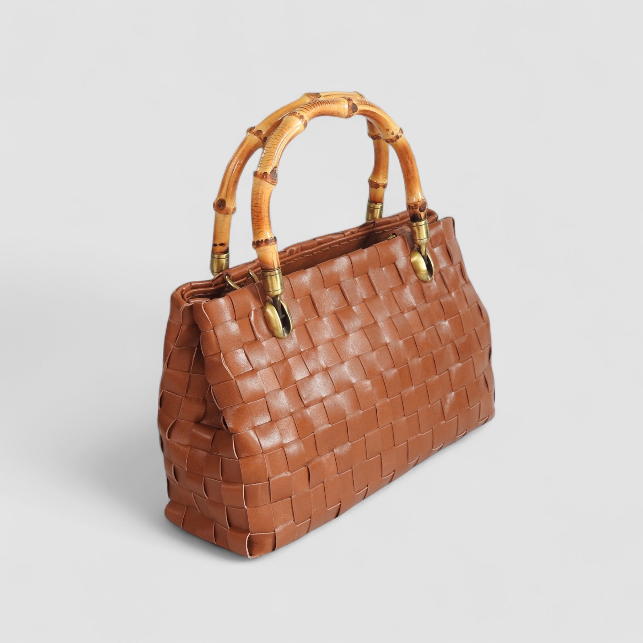 Flettet skinnveske i fargen cognac fra Ribichini med et unikt bambus håndtak og gulldetaljer, bilde er tatt på skrå.