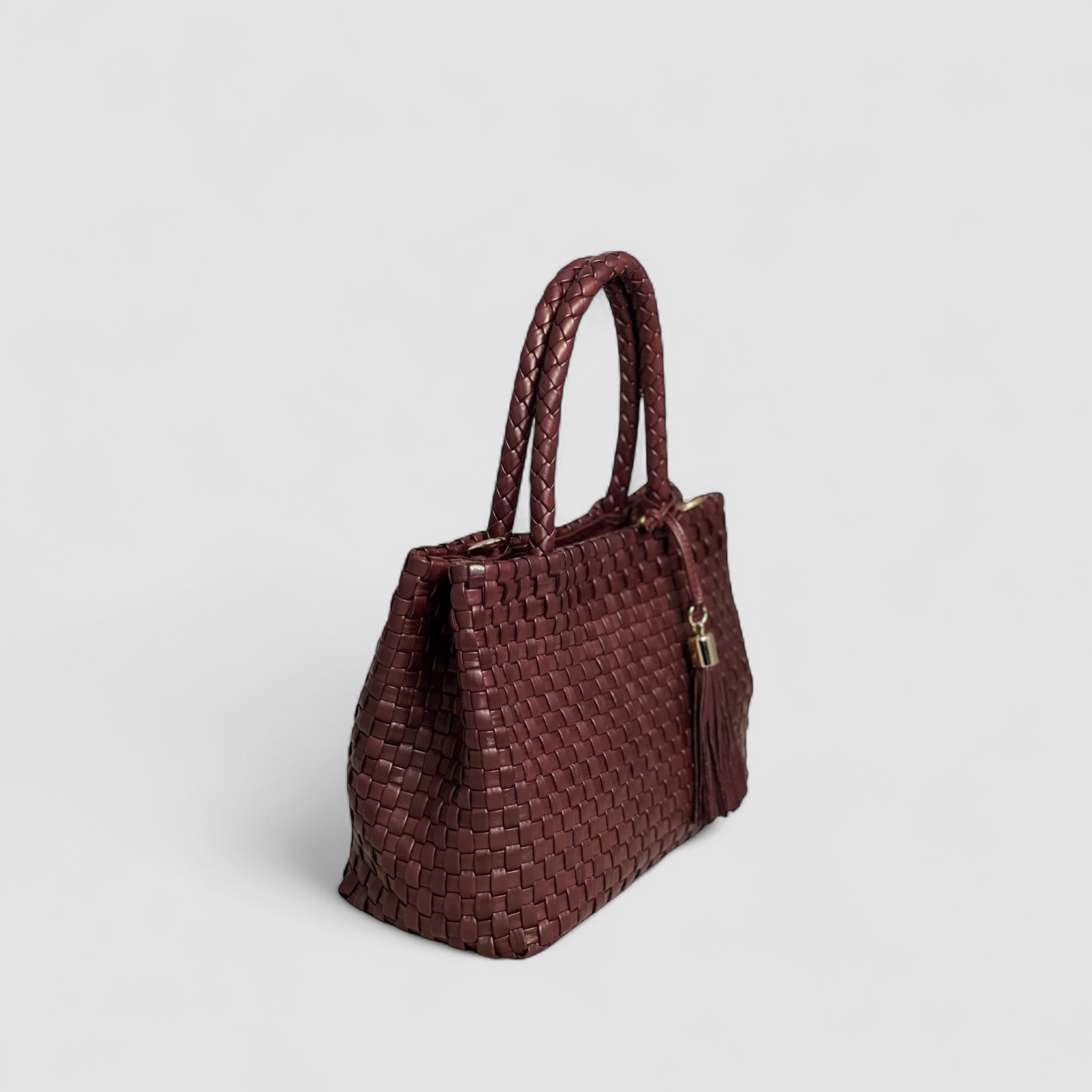 Ribichini Ginny-skinnvesken i flettet bordeaux har en elegant profil med luksuriøse gulldetaljer og en dekorativ dusk.