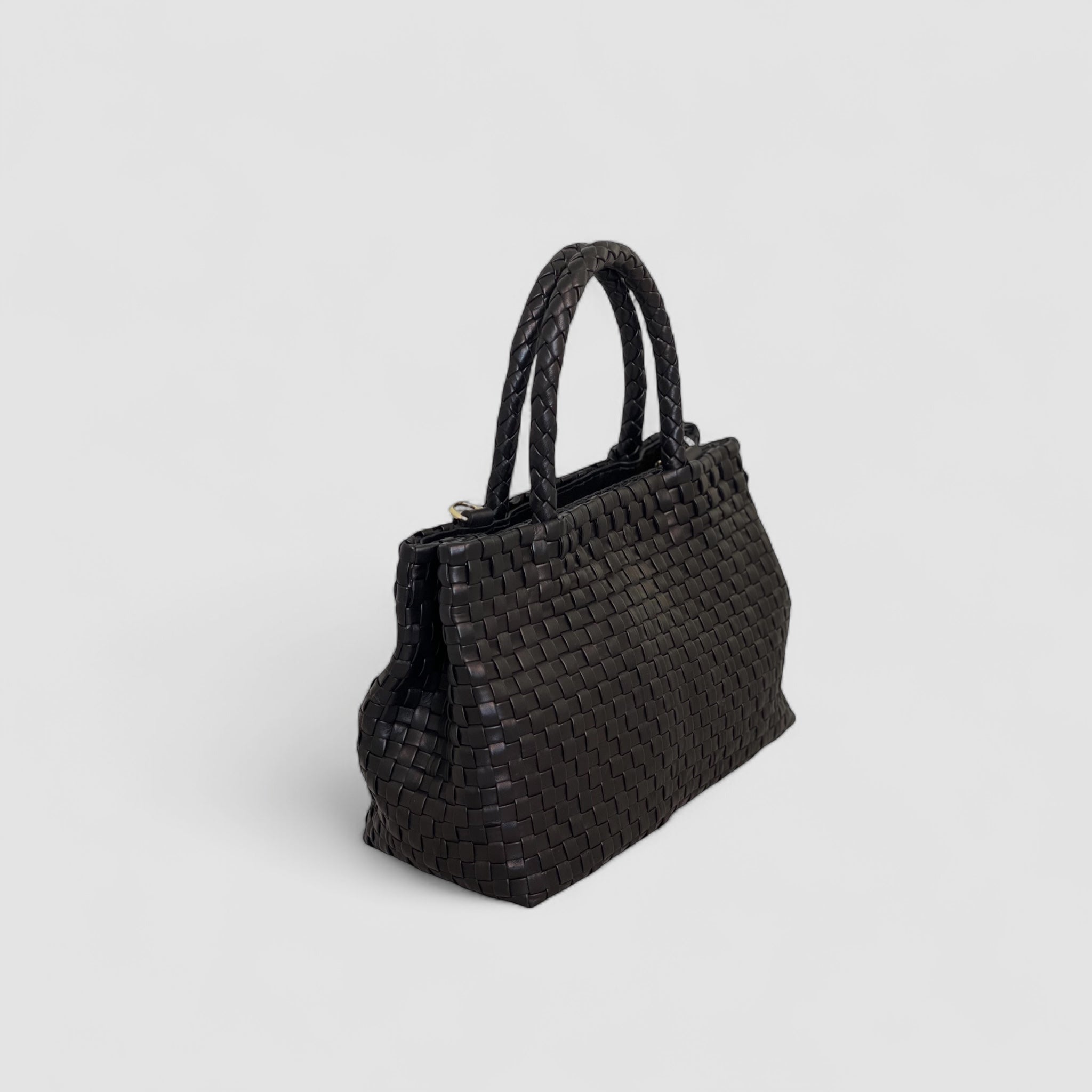 Ribichini Ginny-skinnvesken i flettet sort lammeskinn har en elegant profil sett fra siden, med luksuriøse gulldetaljer og en dekorativ dusk.