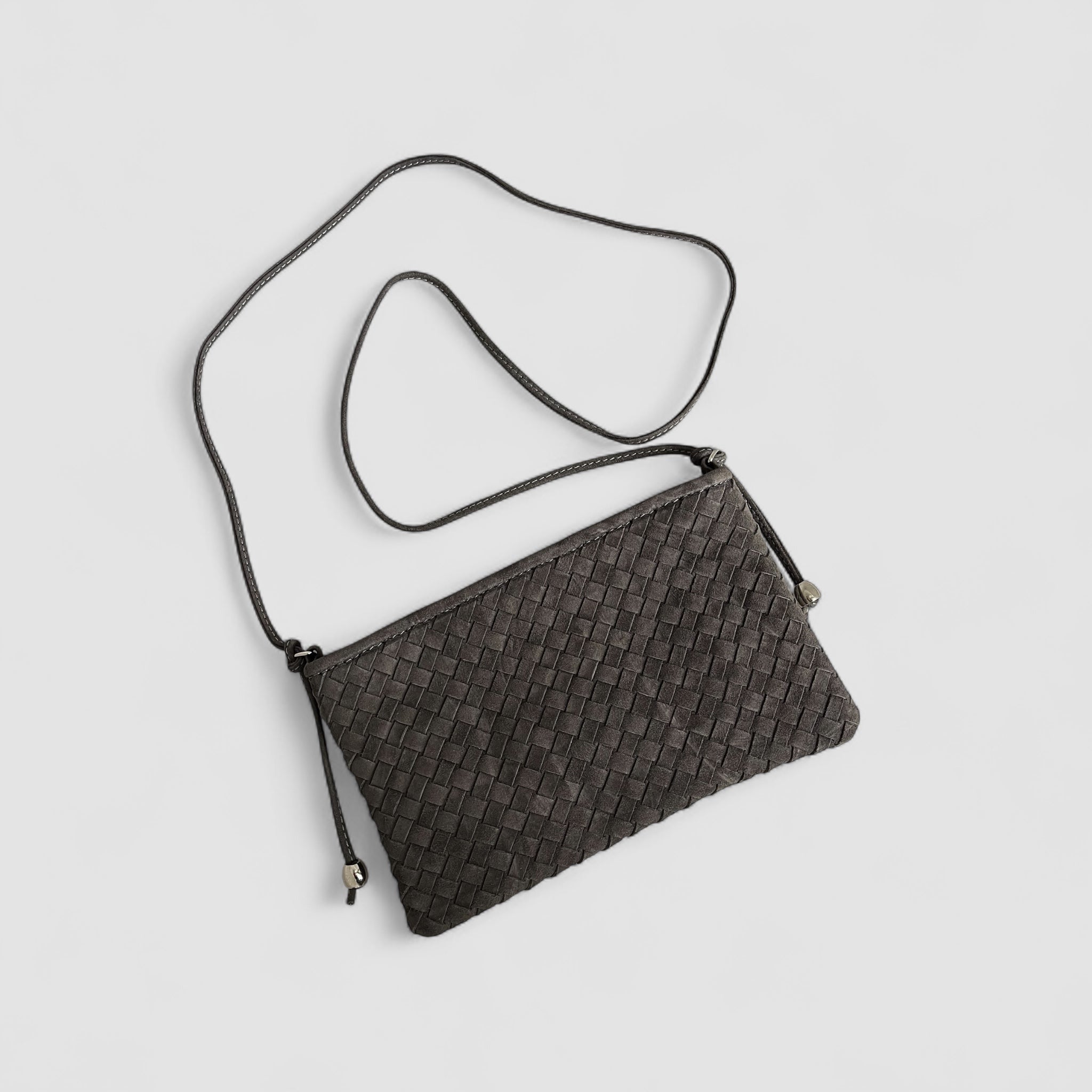 Ribichini Camper clutch i graphite. Den er laget av semsket lammeskinn, har et flettet design og sølvdetaljer, med en justerbar skulderstropp.