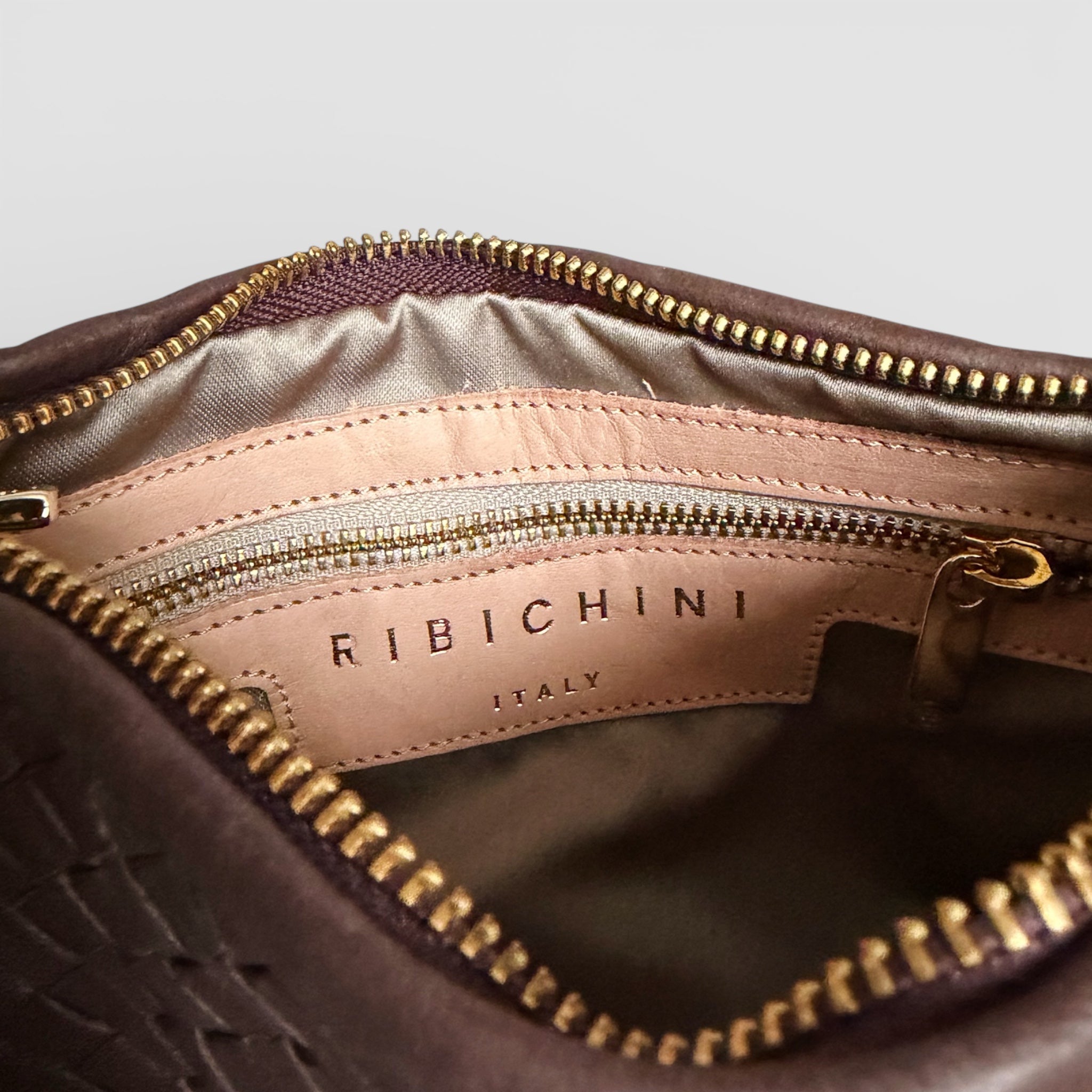 Nærbilde av interiøret på en Ribichini Isola Bella veske, med gullglidelås og skinnmerke som viser "Ribichini Italy