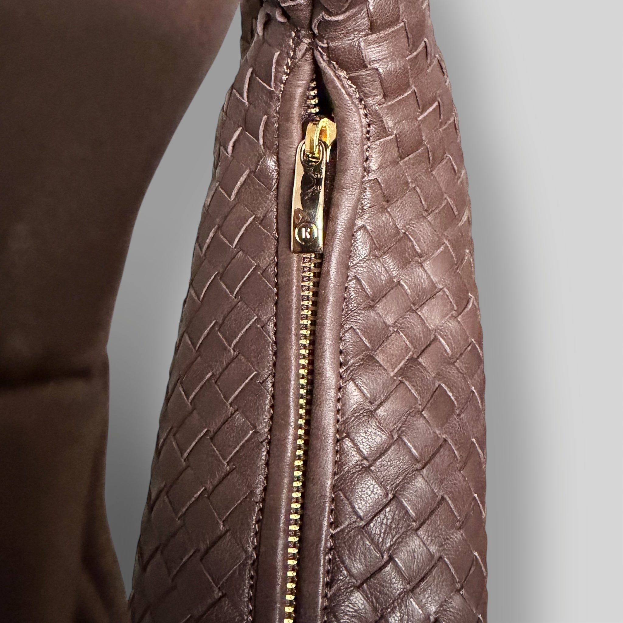 Nærbilde av glidelåsdetalj i gull på en håndflettet Ribichini Isola Bella veske i brun, laget av italiensk skinn.