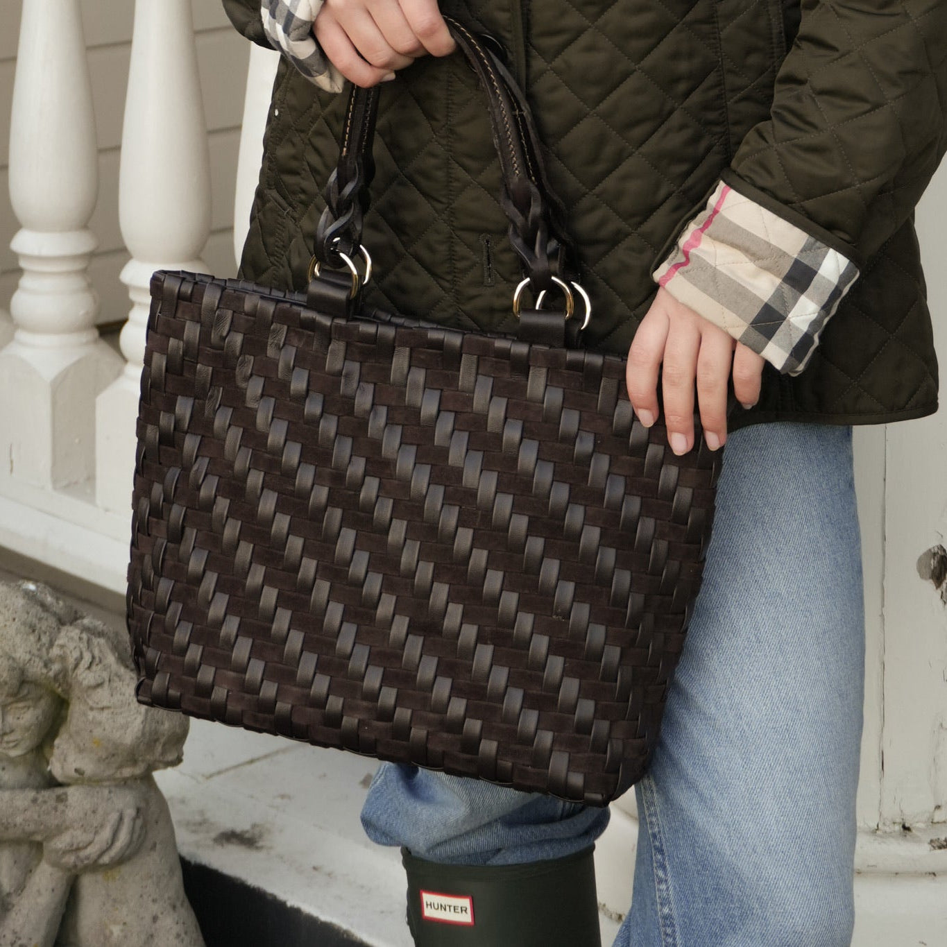 Person i grønn vattert jakke og jeans med Safari Lady Royal Chocolate, en håndflettet mørk brun skinnveske.