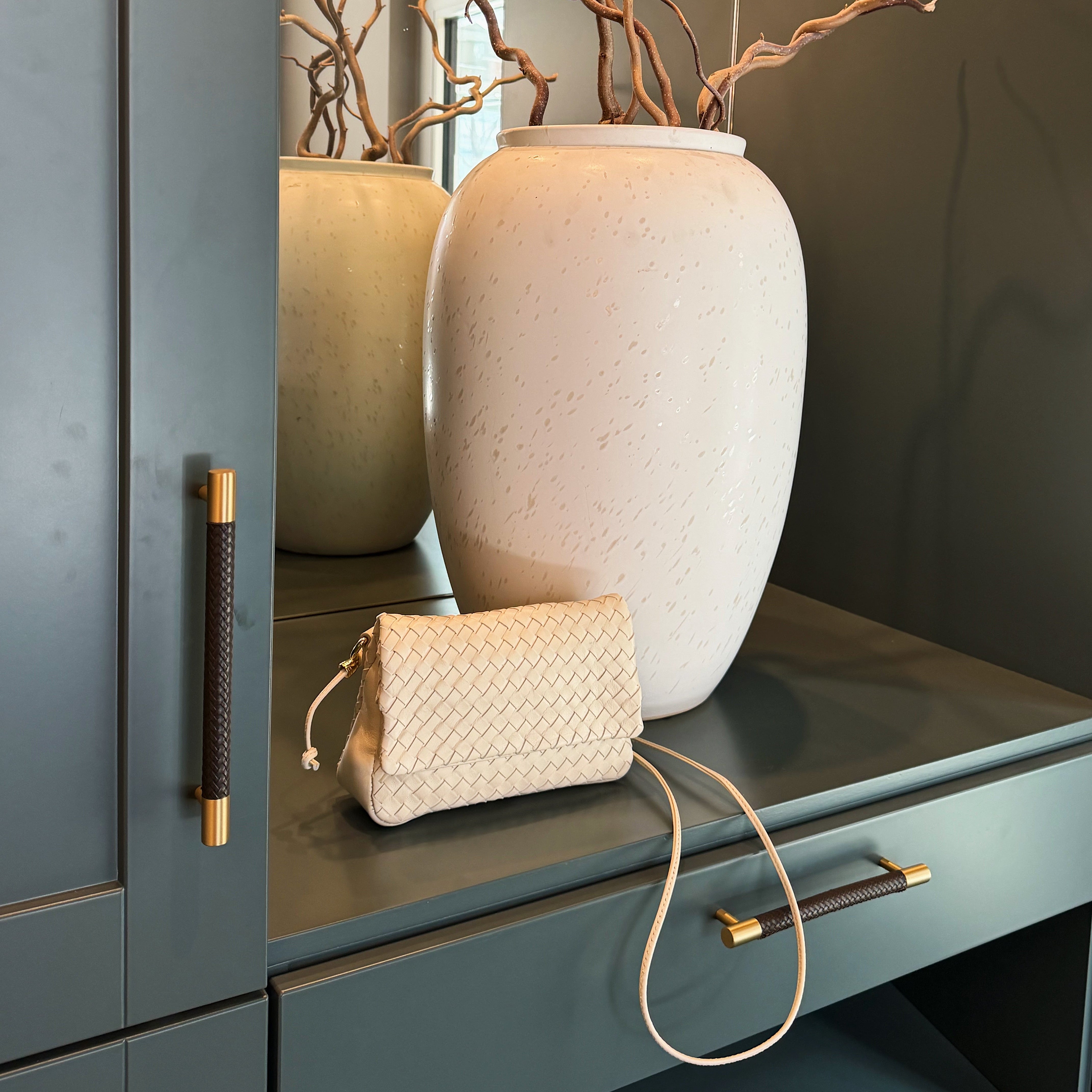 Ribichini Undercover håndflettet clutch i fargen cream utstilt i en hall.
