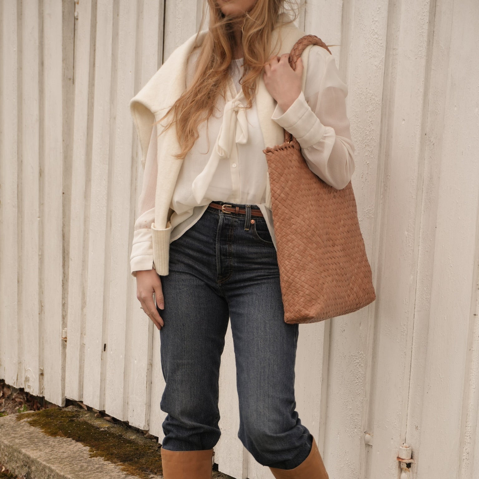 Ribichini Woodstock Cognac håndflettet skinnveske båret over skulderen, stylet med hvit bluse, jeans og brune støvler.