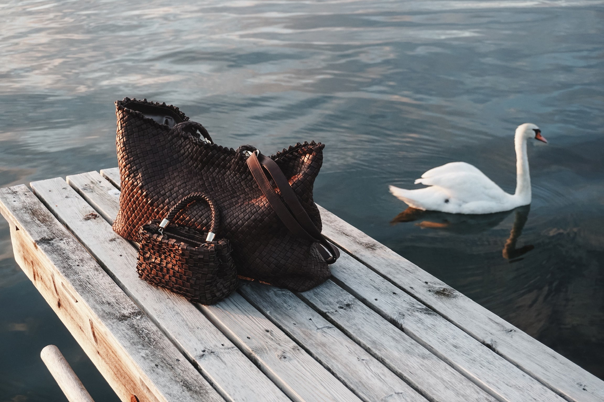 Ribichini håndflettede italienske skinnvesker i mørkebrunt skinn plassert på en brygge ved vannet