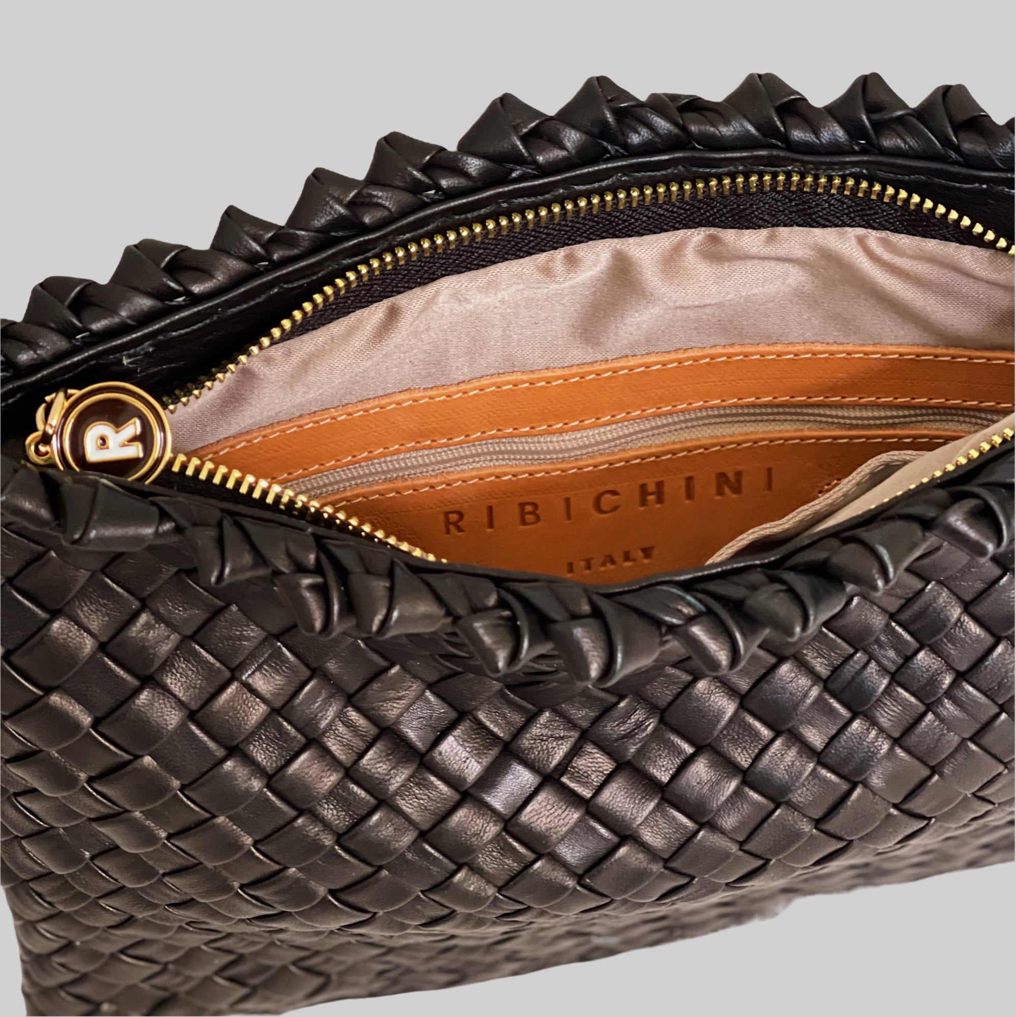 Innsiden av den sorte Ribichini Woodstock-clutchen er praktisk designet med en sikker glidelåslomme for små gjenstander og to åpne lommer for organisert oppbevaring.