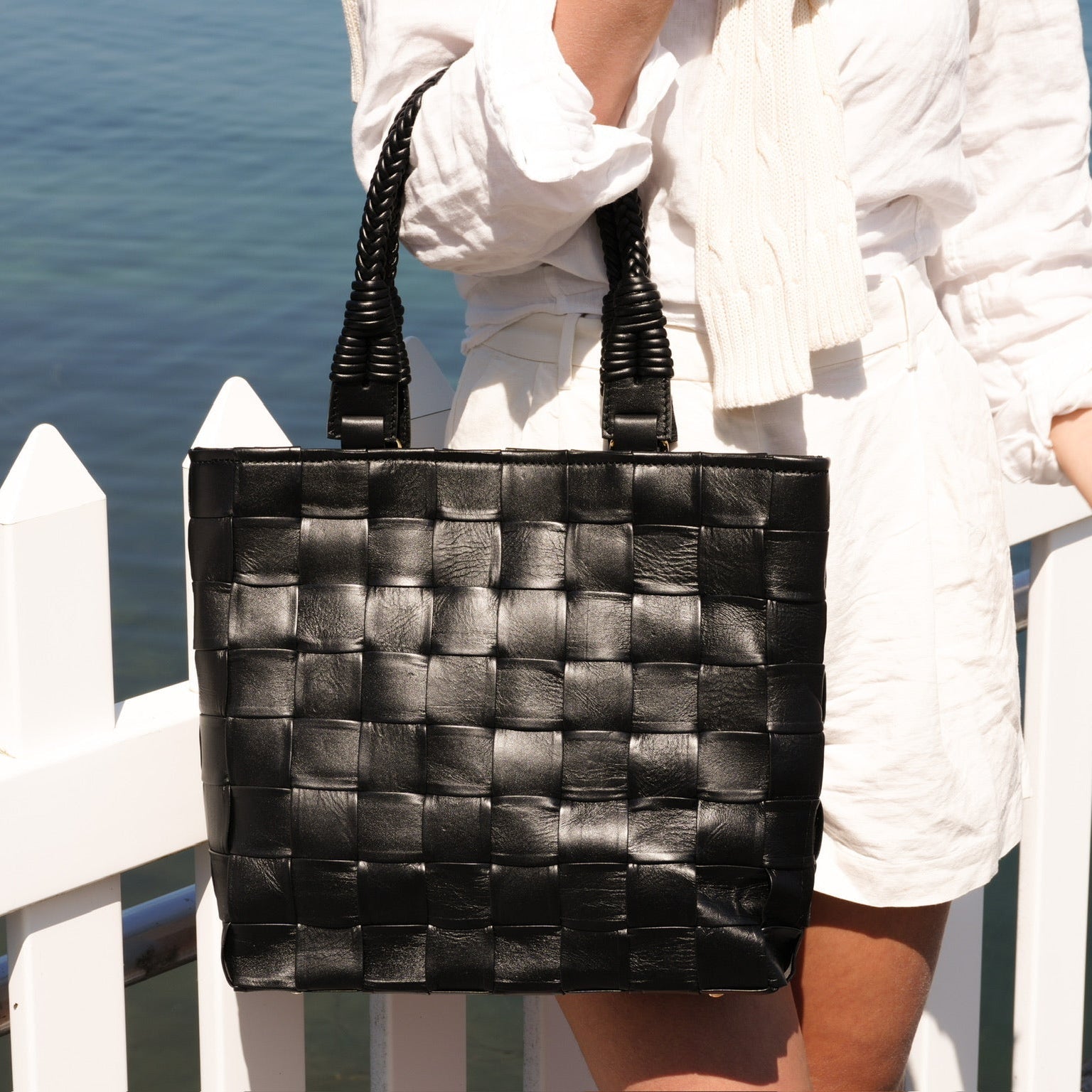 Ribichini Square Babe Black håndflettet toteveske i italiensk lammeskinn ved sjøen.