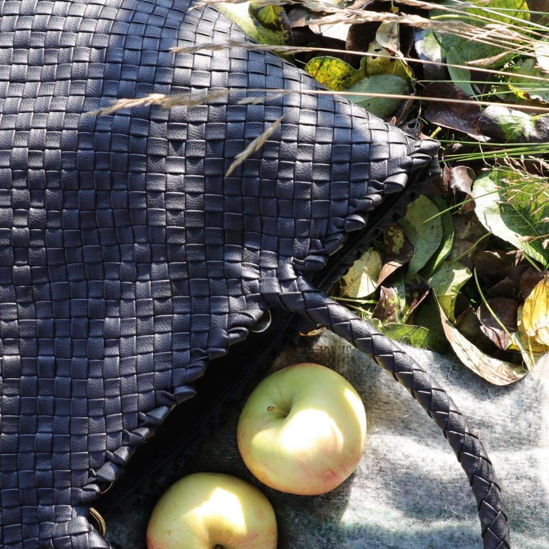 Vakker flettet sort veske, laget av eple skinn, og to friske epler som er plassert ved siden av vesken. 
