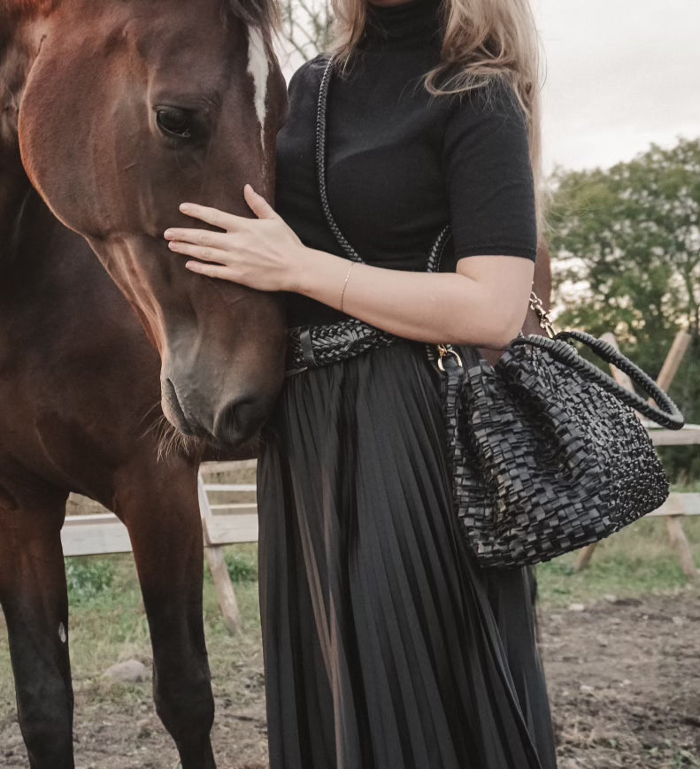 Kvinne klapper en hest og bærer en Ribichini Loren skinnveske i sort.