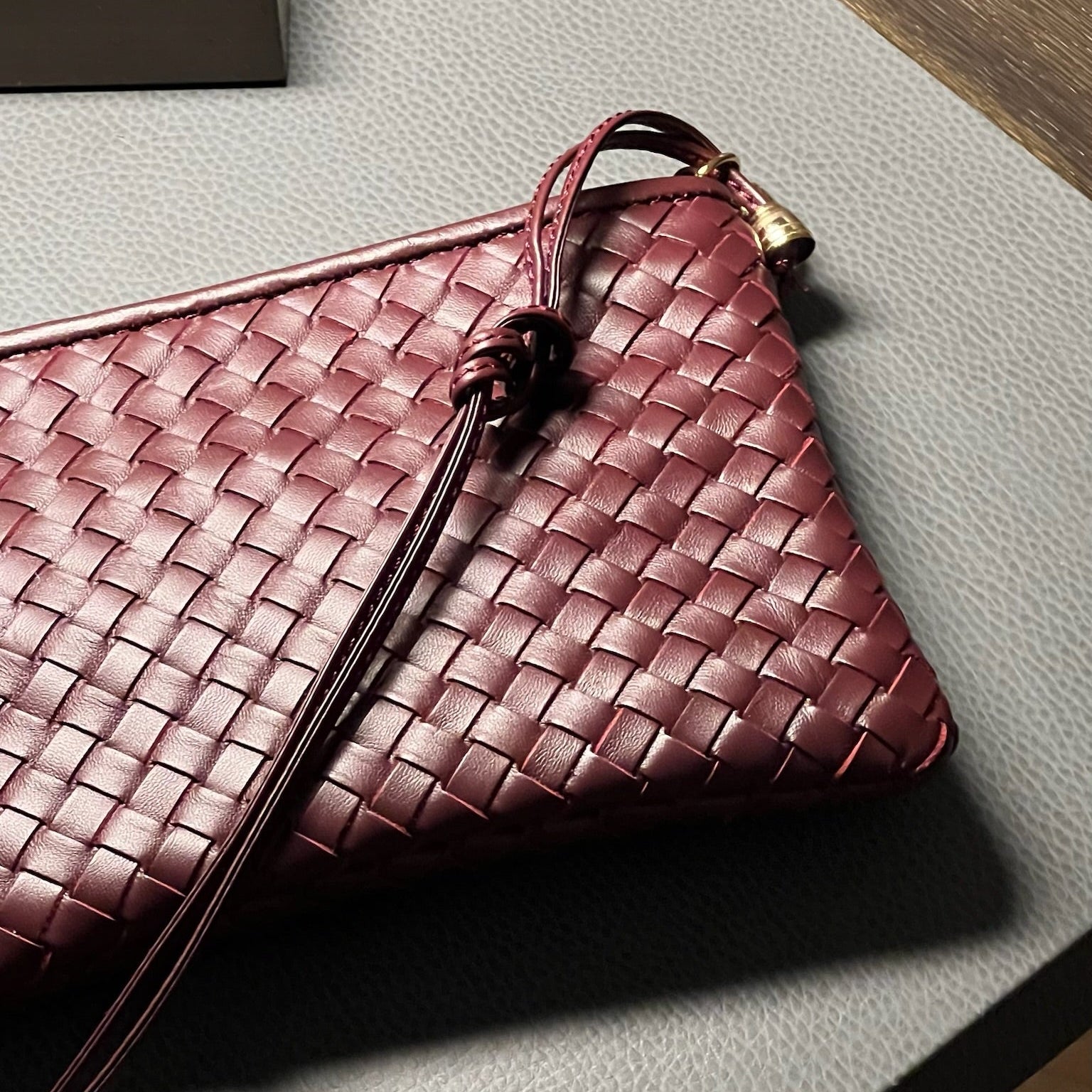 Ribichini Camper Clean Clutch Bordeaux i håndflettet bordeauxfarget lammeskinn på bord, med lang skulderrem og gulldetaljer.