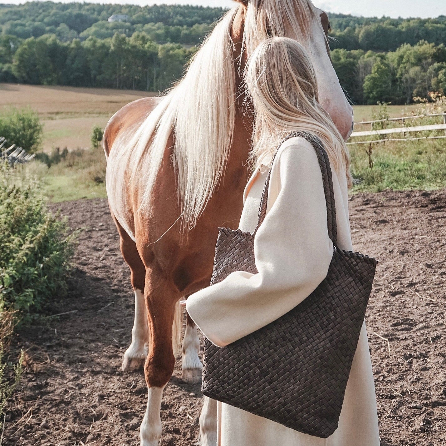 Ribichini Woodstock Hickory – håndflettet brun skinnveske i lammeskinn, stylet med lys kåpe ved hest på landet.