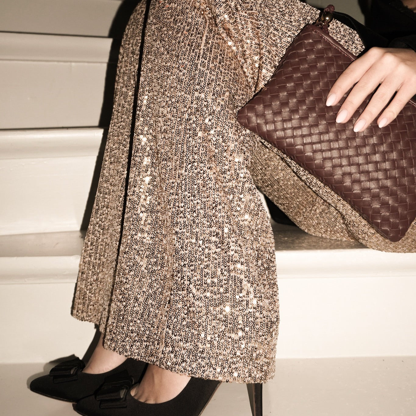 Ribichini Camper Clutch i flettet skinn, stylet med paljettbukser og sorte hæler – elegant kveldslook.