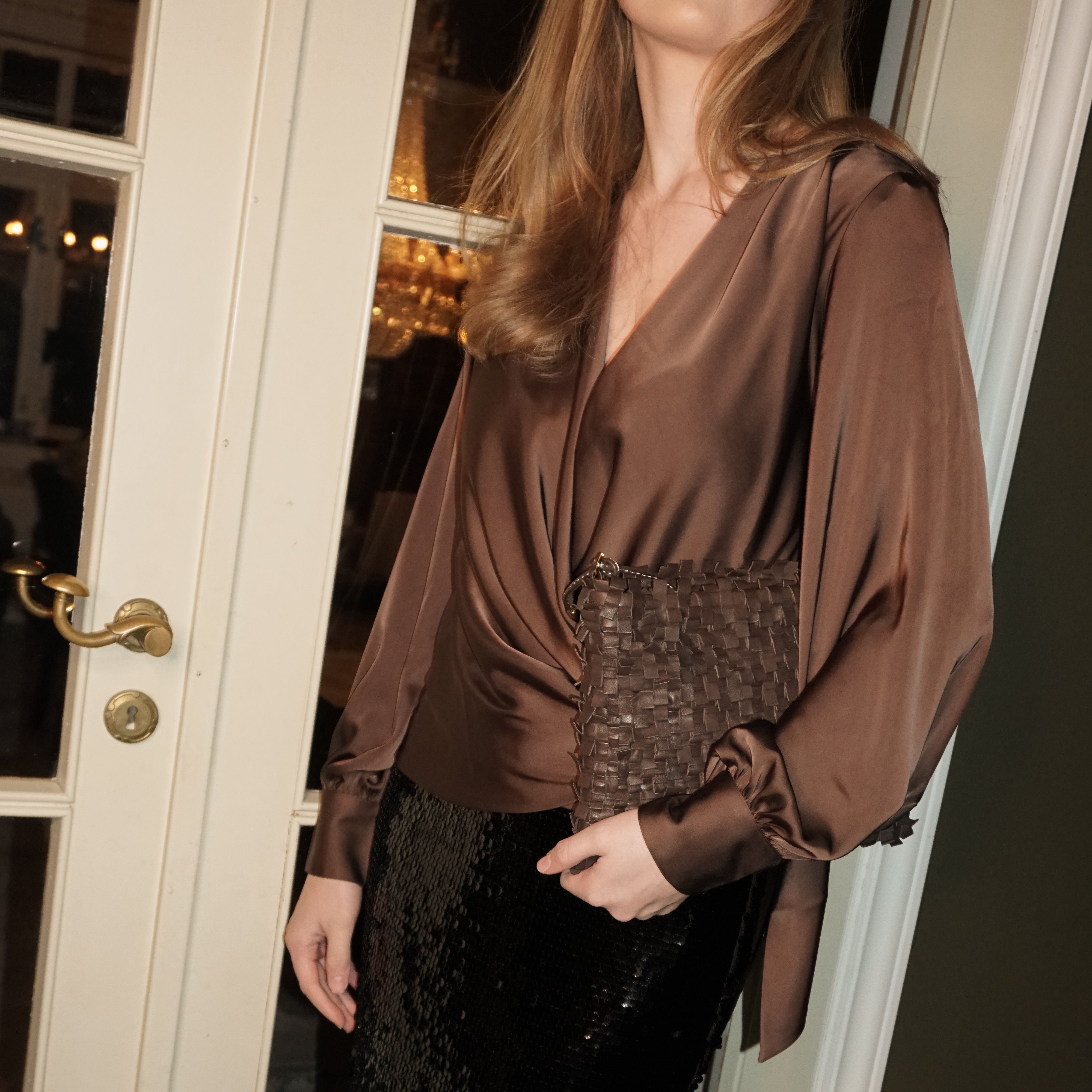 Kvinne i brun silkeshorte holder en Ribichini Loren clutch i flettet brun plisse under armen.