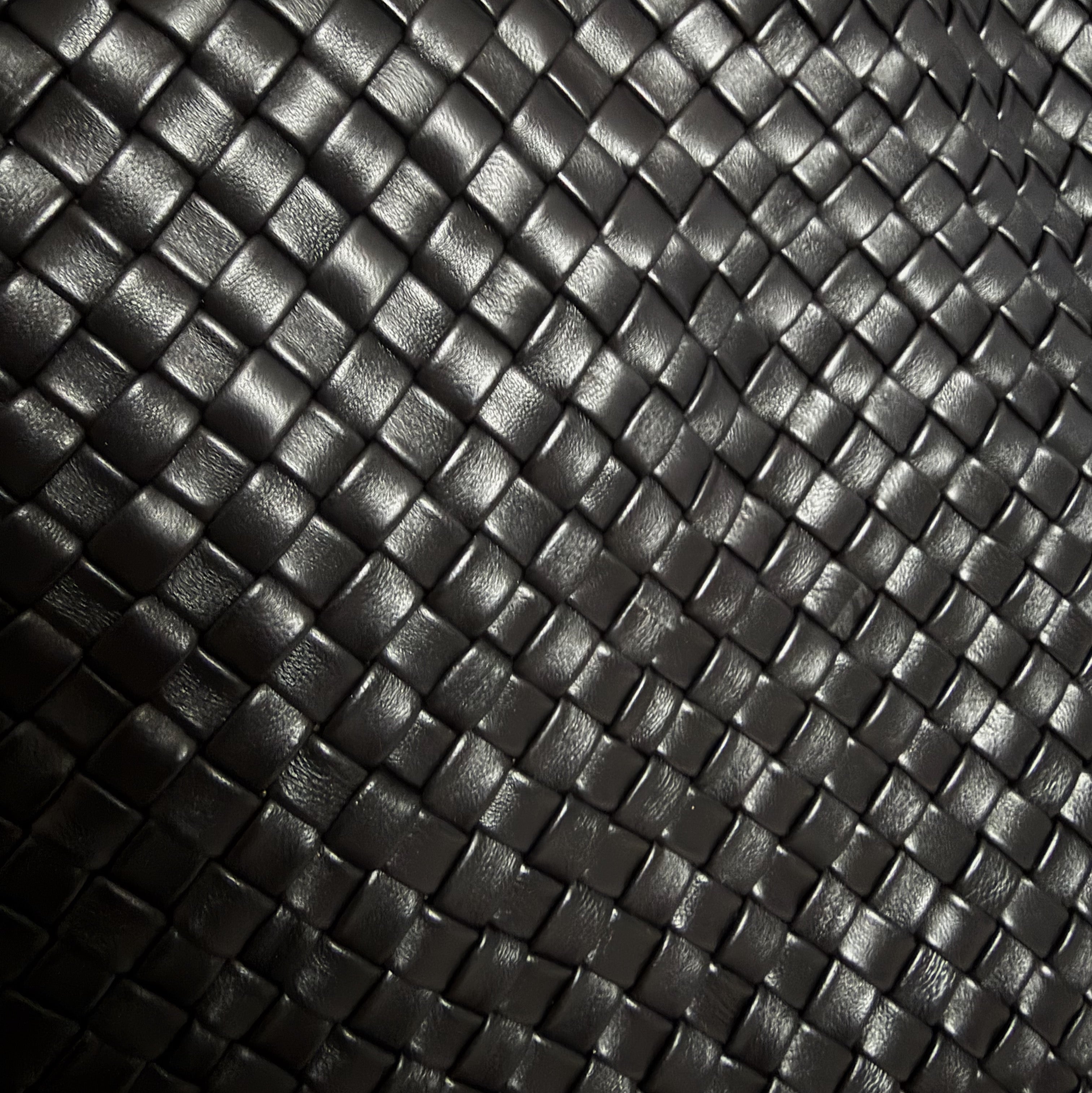 Detaljbilde av håndflettet sort skinn med tett struktur og myk overflate.